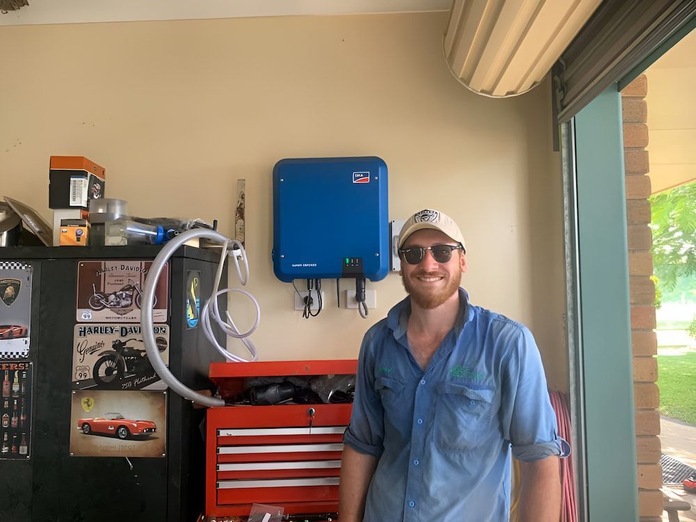 A Man Is Standing In A Garage With A Solar Panel On The Wall — Levi's Electrics in Nerimbera, QLD