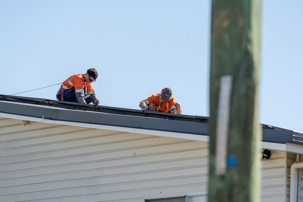 2 Men Are Working On A Solar Panel On A Roof — Levi's Electrics in Gladstone, QLD