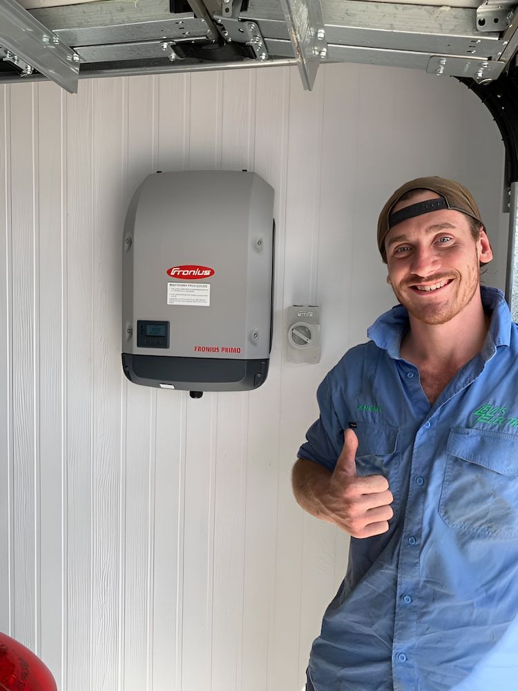A Man Is Giving A Thumbs Up In Front Of A Solar Inverter — Levi's Electrics in Emerald, QLD