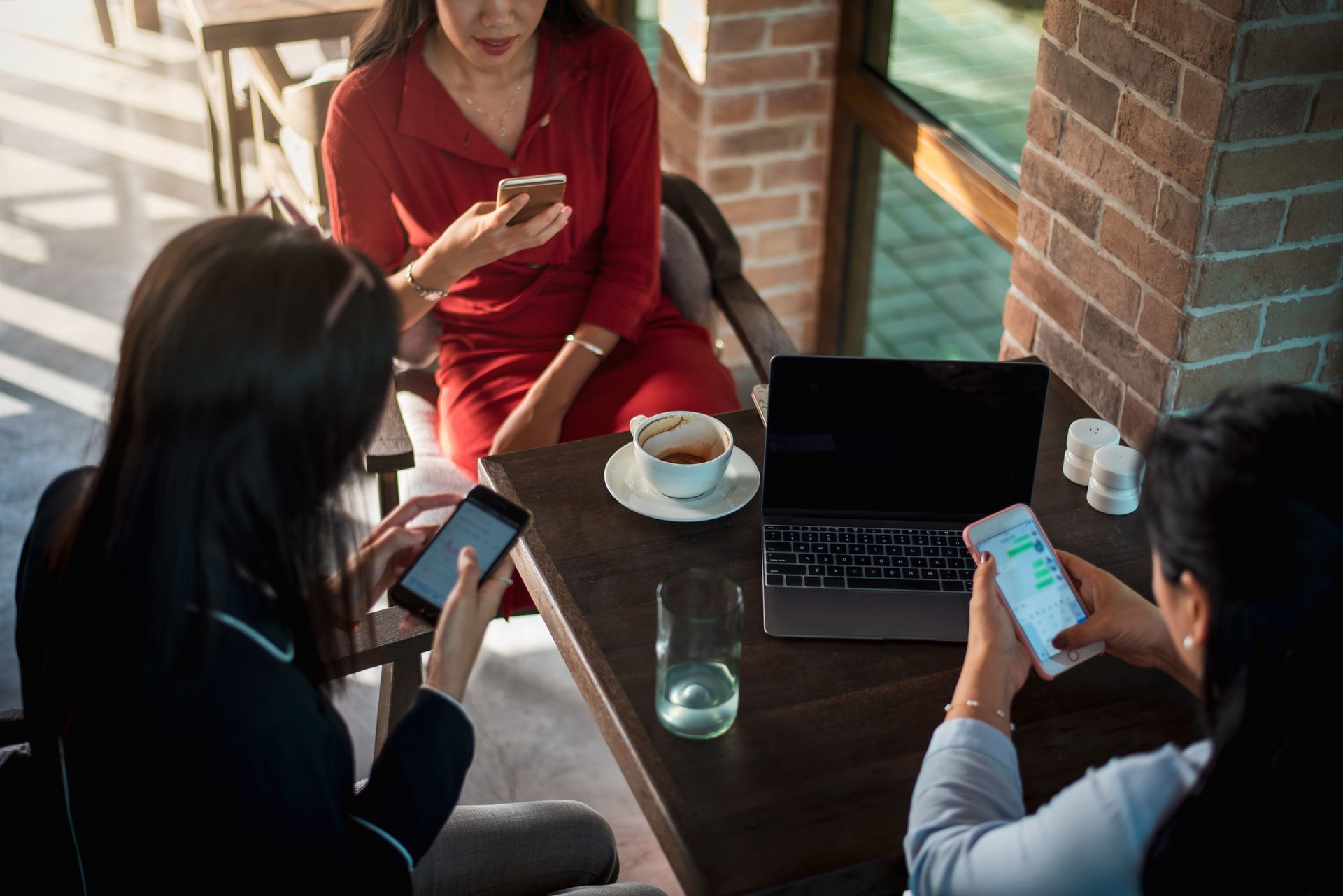 Three women are sitting at a table looking at their phones.