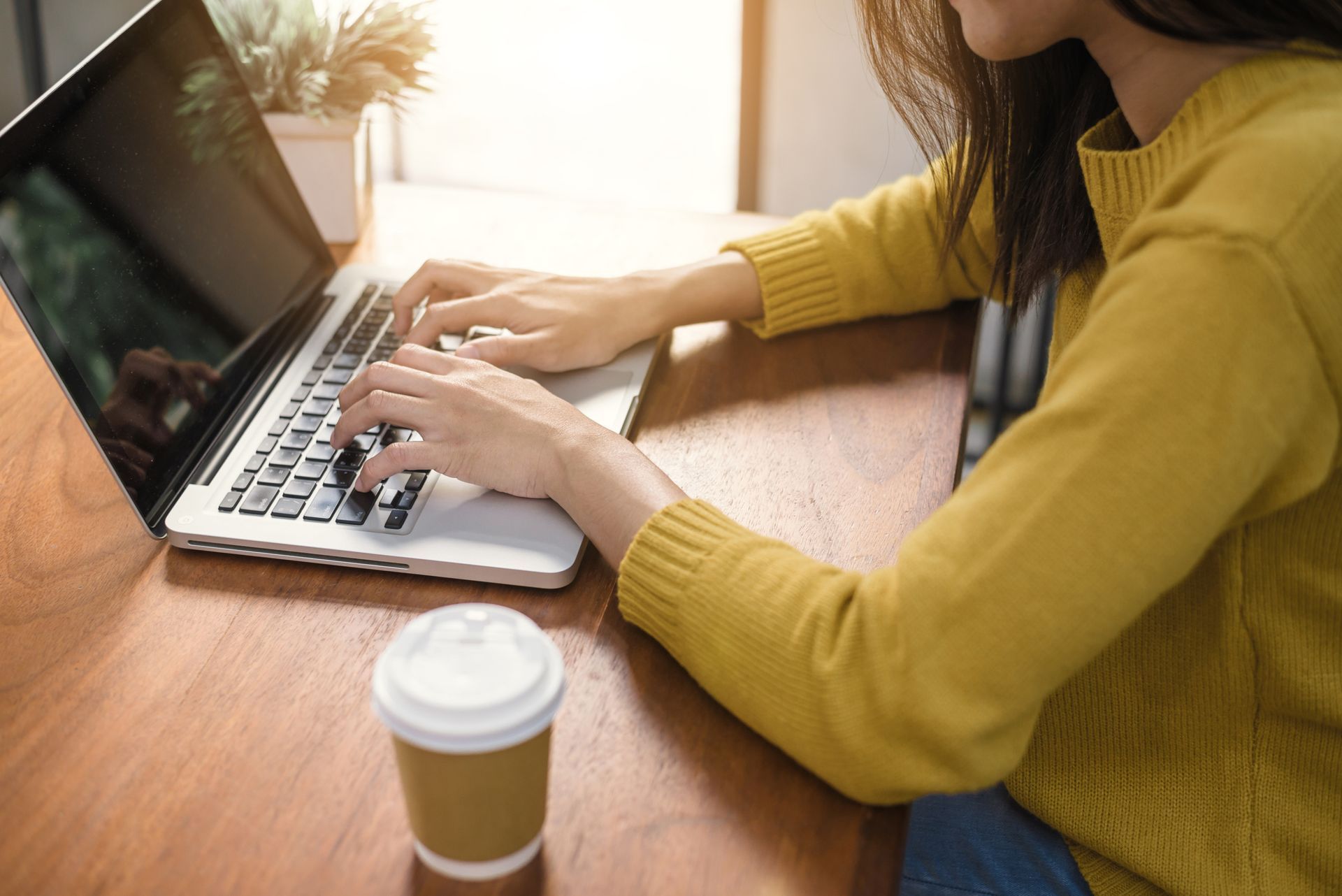 A woman in a yellow sweater is typing on a laptop computer.