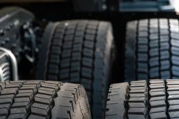 Close-up of large black truck tires stacked in a row, with a vehicle visible in the background.
