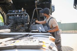 Technician working on machinery in the back of a truck, inspecting hoses with tools nearby