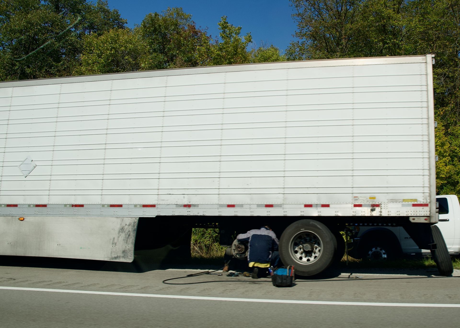 White semi-truck trailer stopped on roadside with a person working underneath it