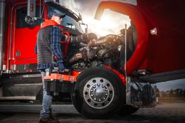 Truck driver inspecting engine of a red semi-truck at sunset