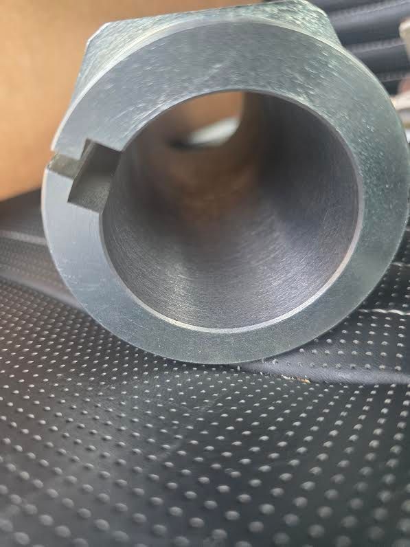 Close-up of a gray metal cylindrical part with a small notch, resting on a textured black surface.