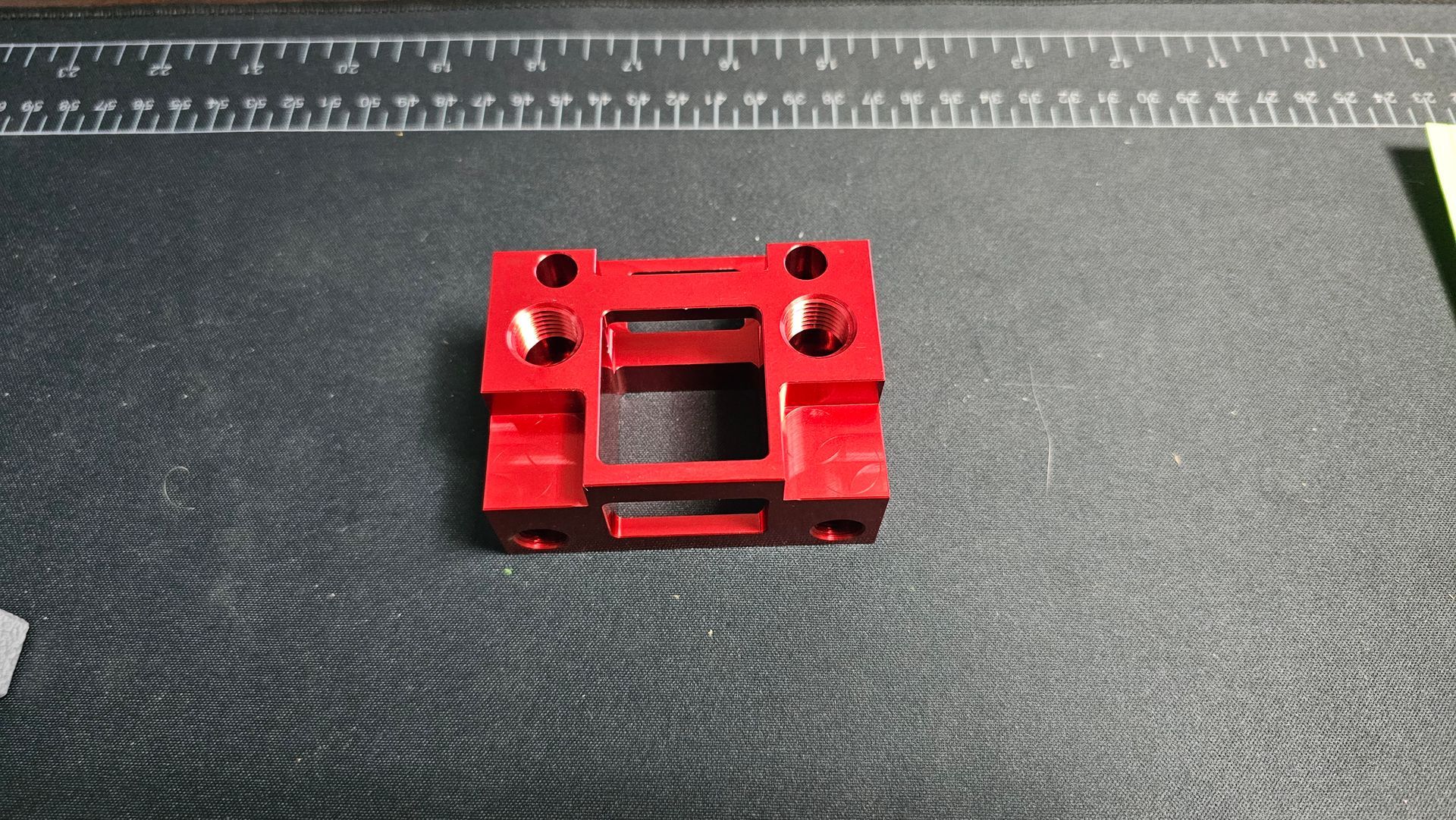 Red metal bracket centered on a dark textured surface, with holes and a rectangular cutout.