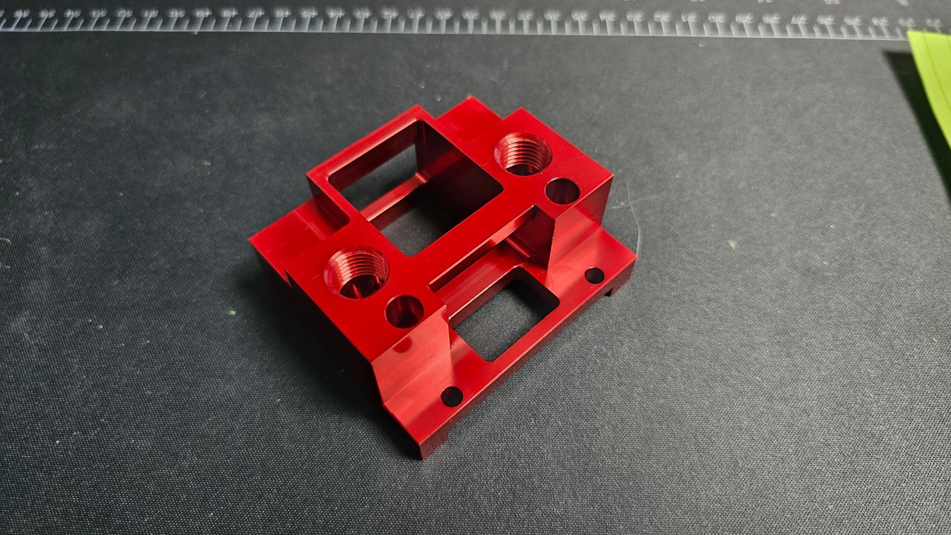 Red anodized metal bracket or mounting part on a dark textured surface.