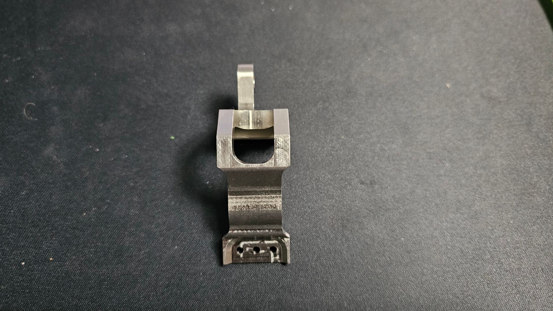 Small worn metal clamp or bracket centered on a dark textured surface.