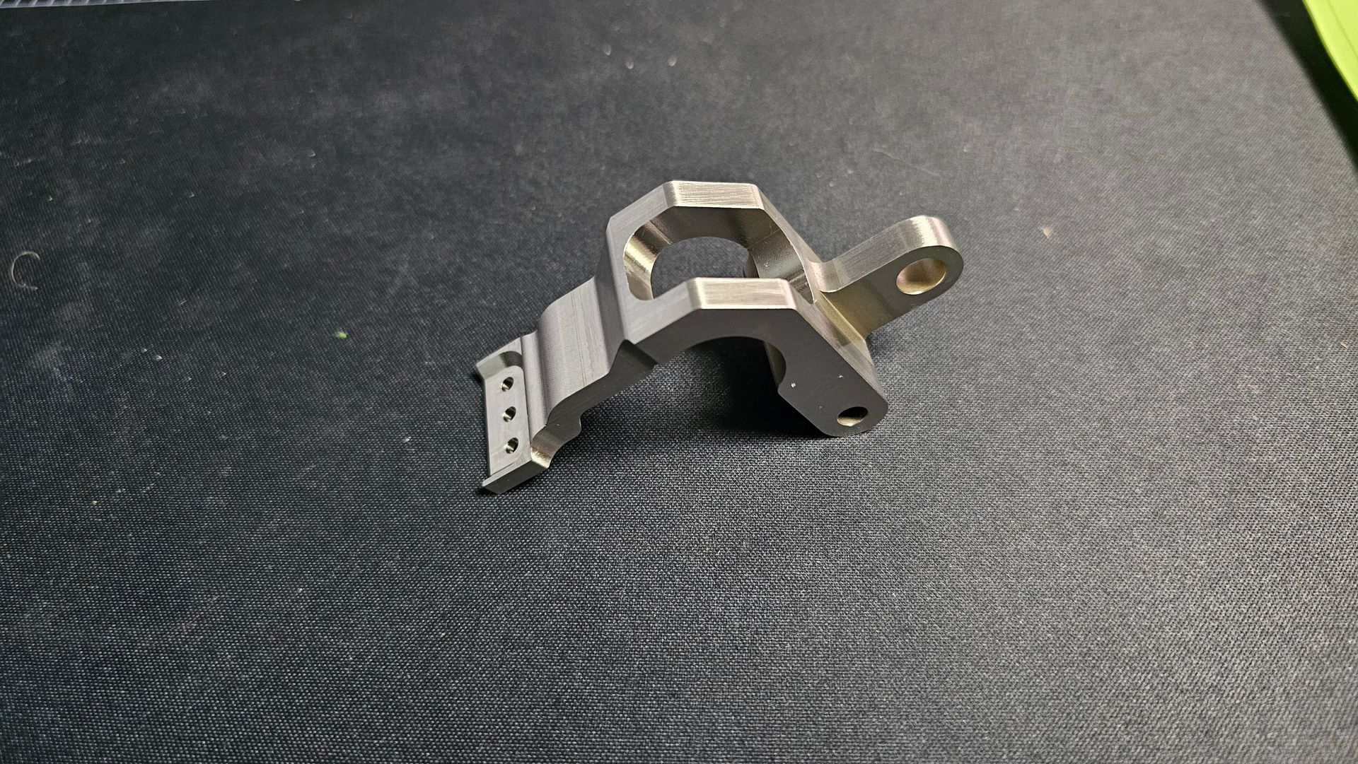 Small silver metal bracket lying on a dark textured fabric surface