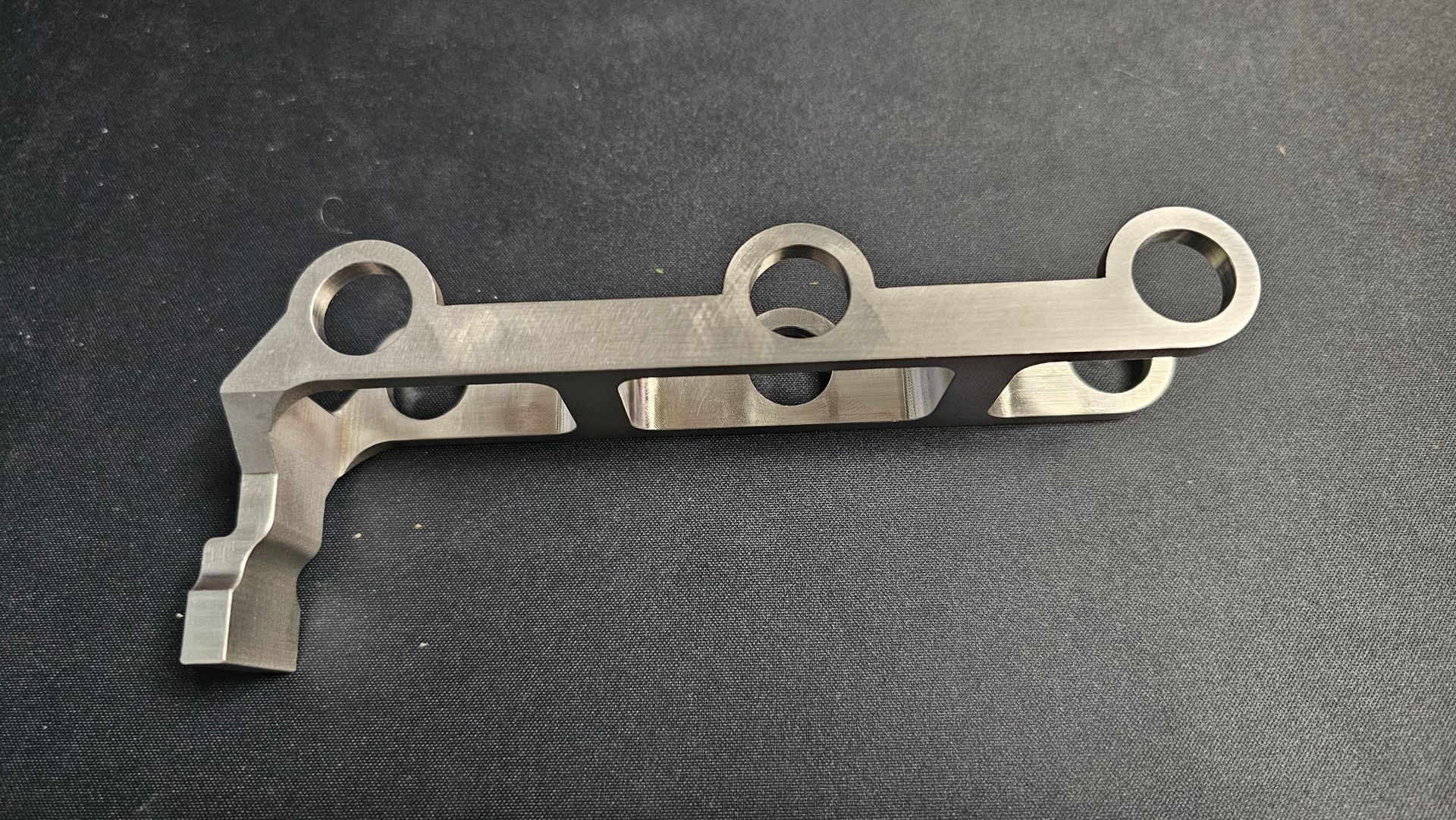 Metal mechanical bracket with three circular holes on a dark textured surface