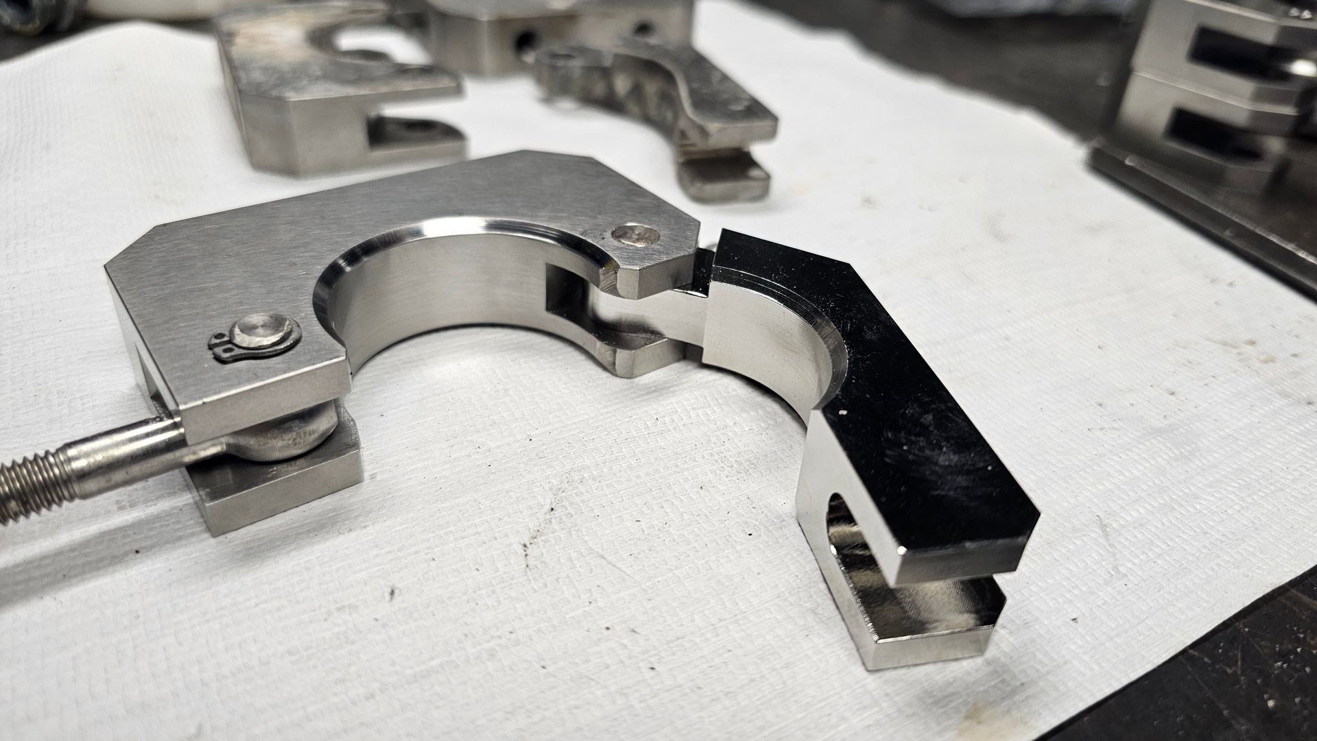 Metal mechanical clamp and bracket parts on a workbench, with a black lever attached