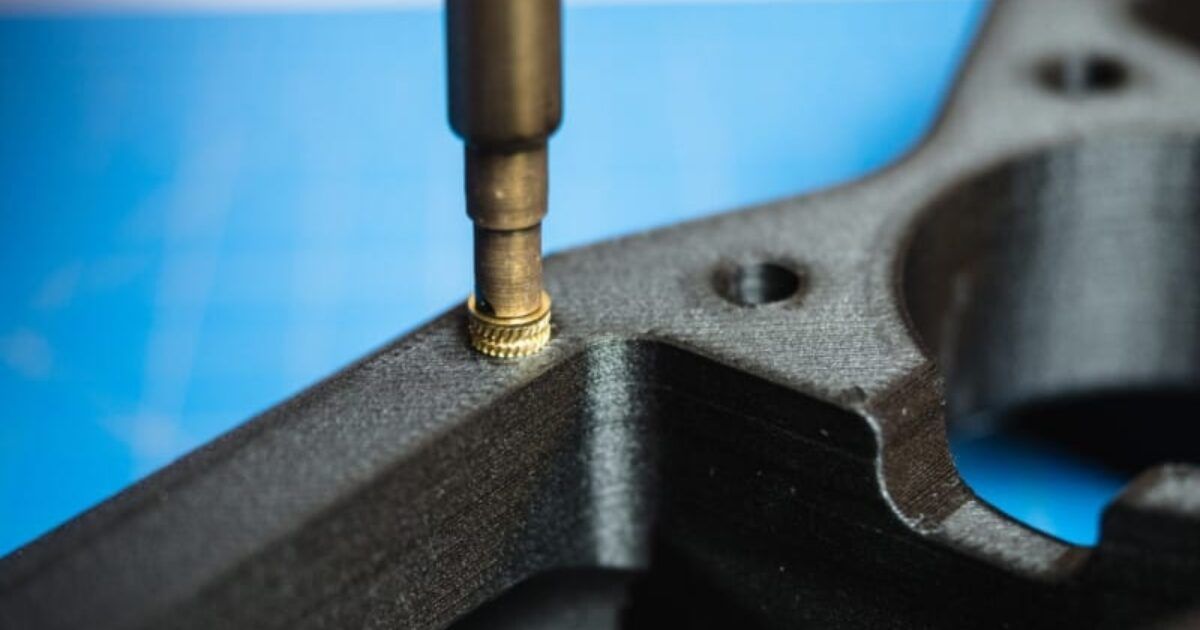 A tool inserting a brass threaded insert into a black plastic part.