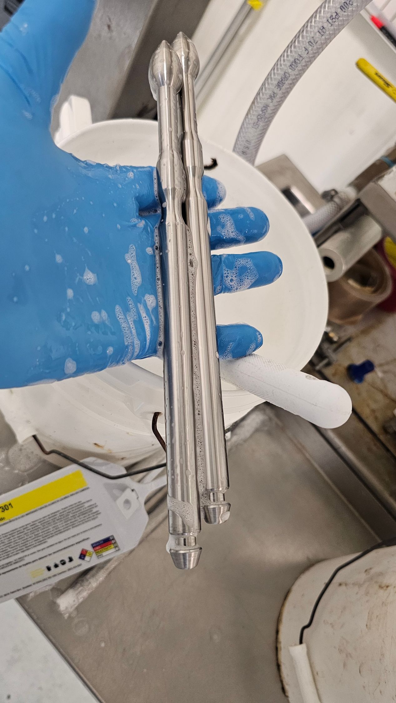 Blue-gloved hand holding a clear cylindrical tube in a laboratory setting