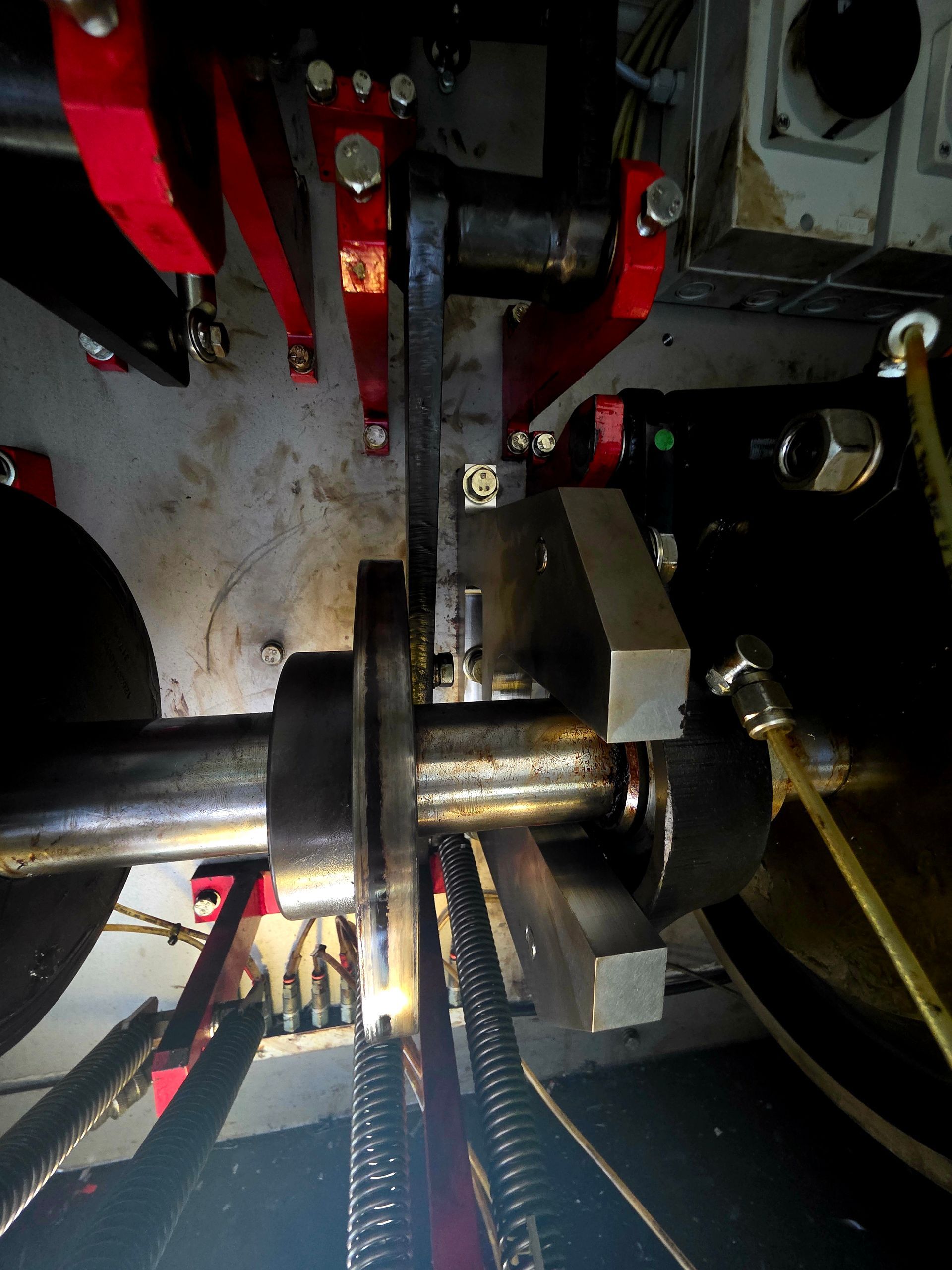 Close-up of industrial machinery with red metal arms, a central shaft, and cables in a dim workspace