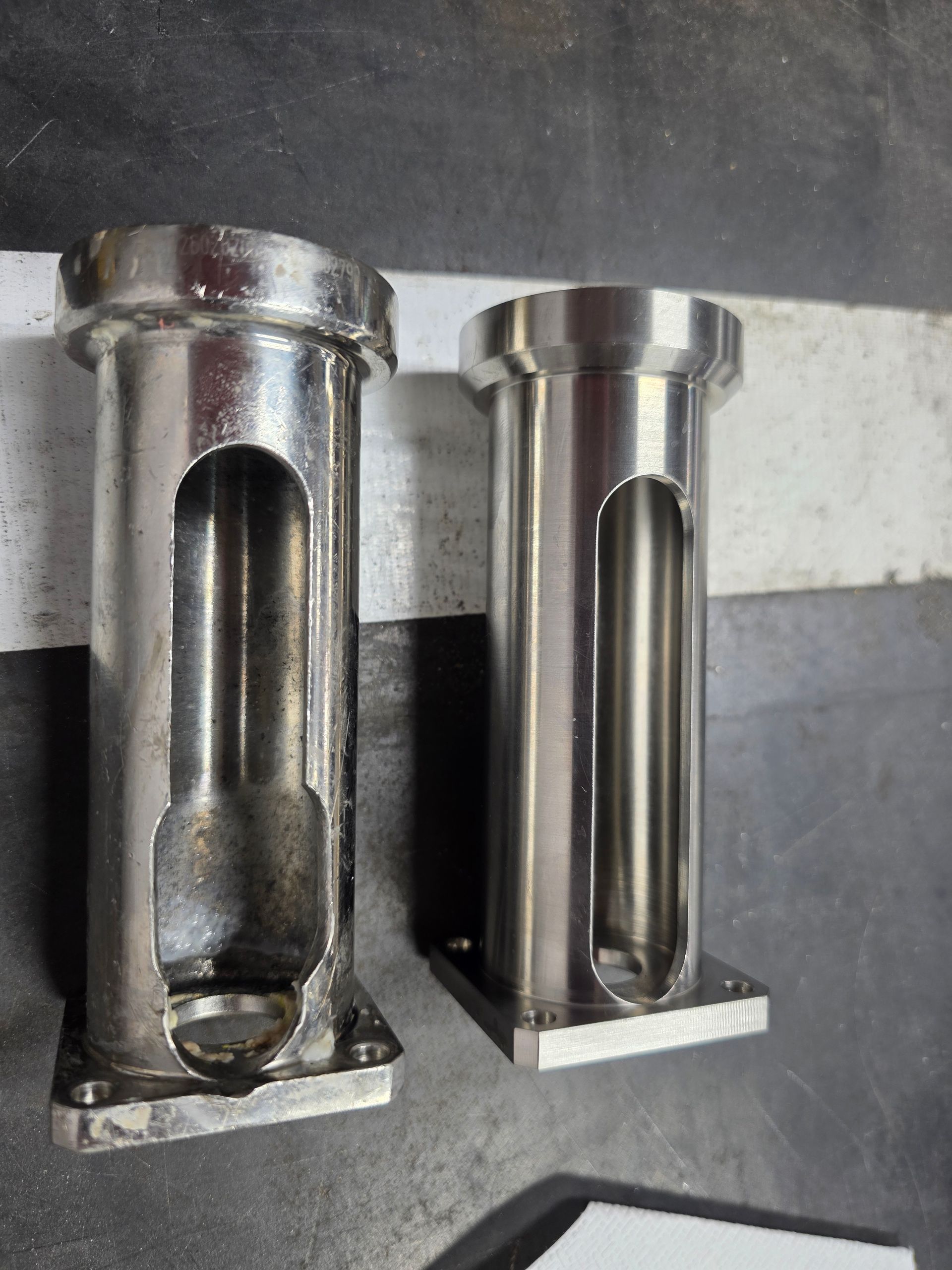Two metal cylindrical parts with vertical slots, standing side by side on a dark surface.