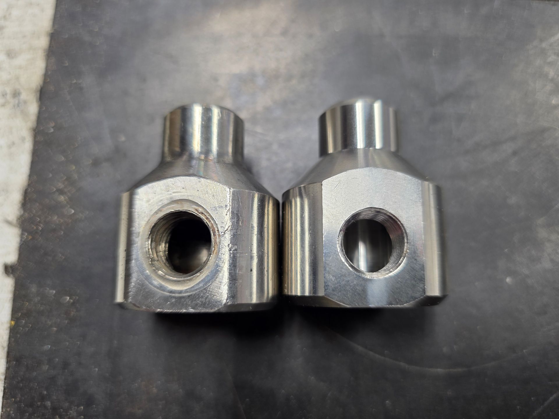 Two silver metal machined parts side by side on a gray surface