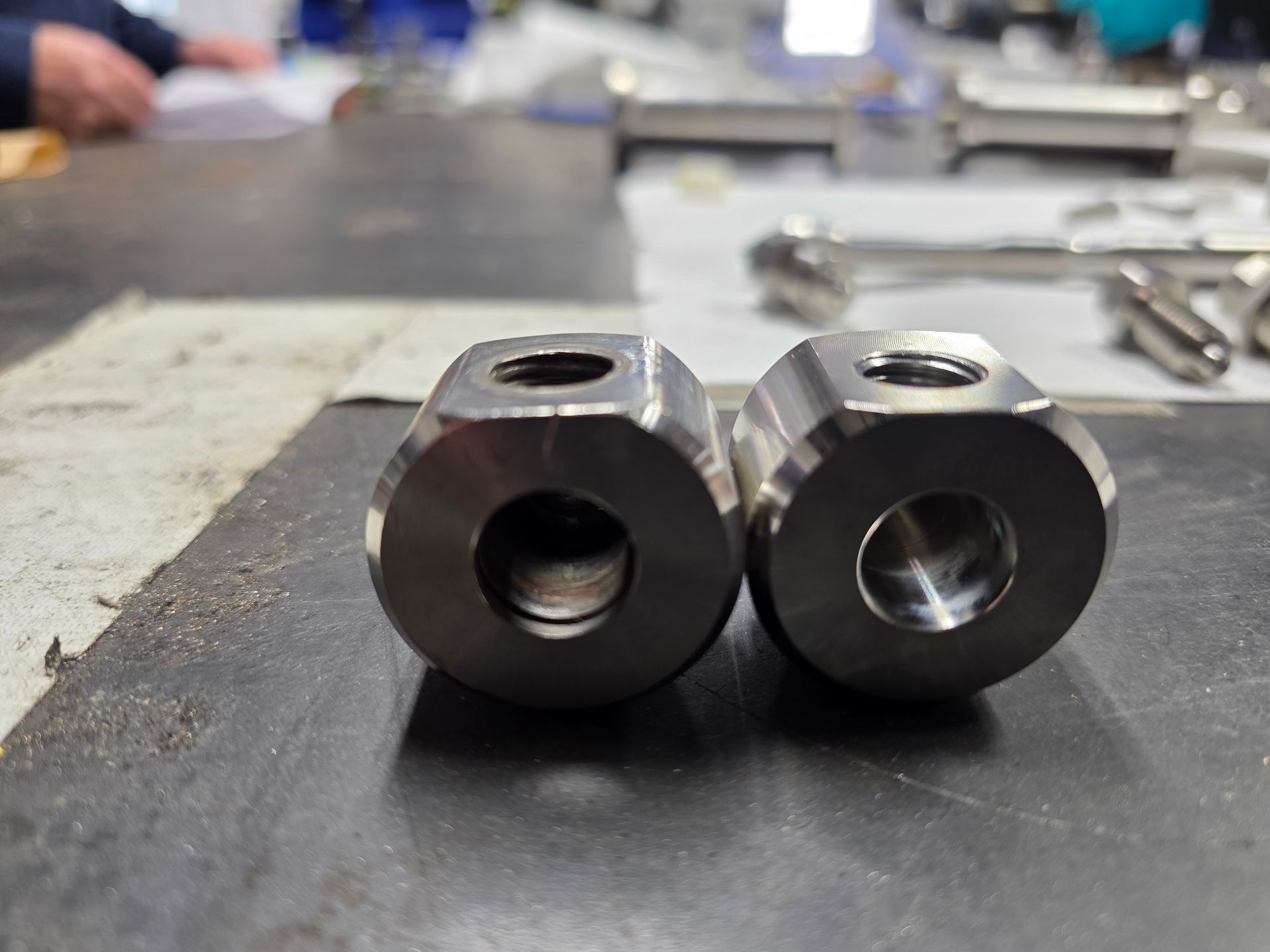 Two metal machined parts with central holes sitting on a workbench in a workshop