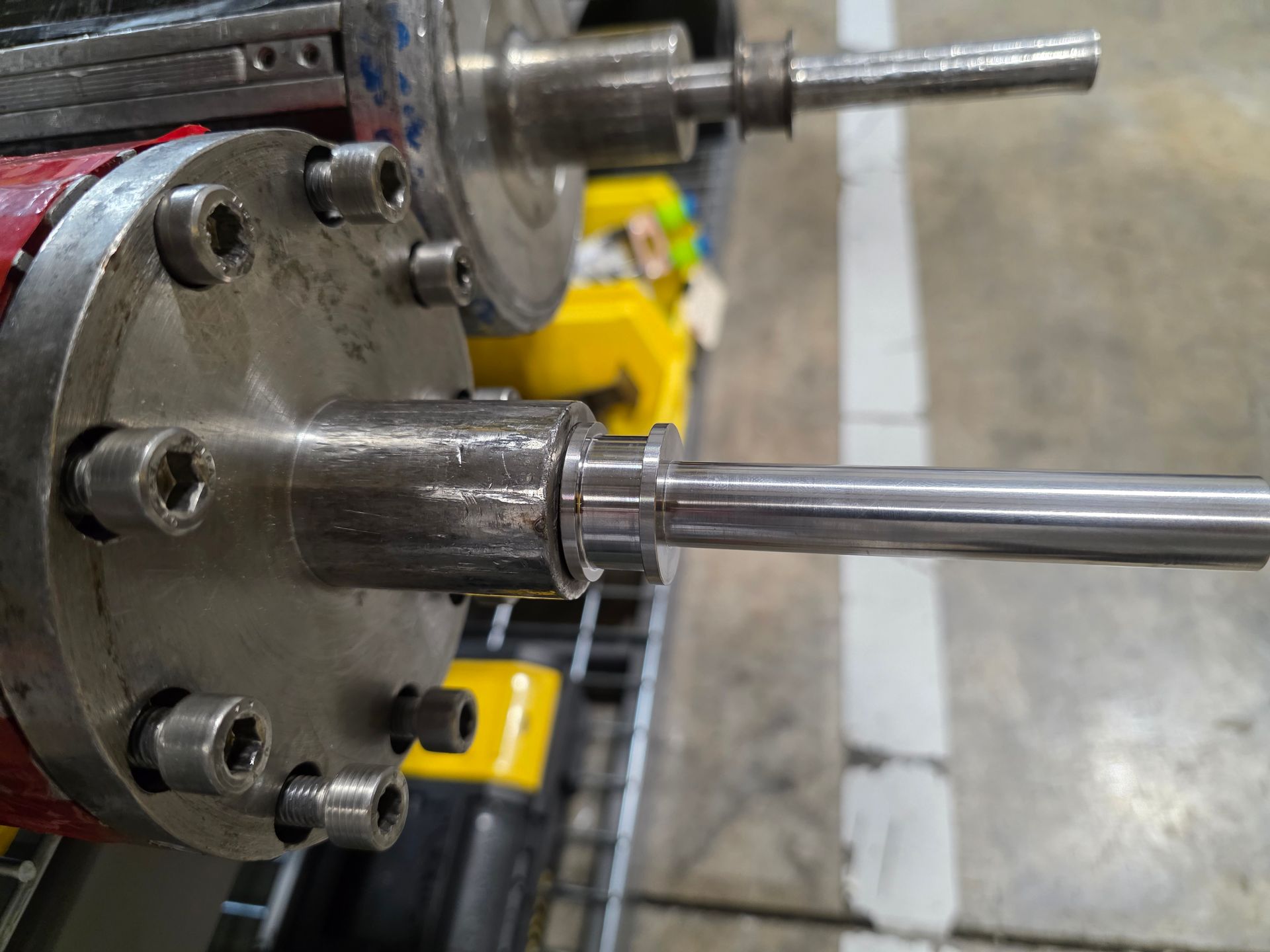 Close-up of a metal machine shaft and flange in an industrial workshop, with bolts and polished rods.
