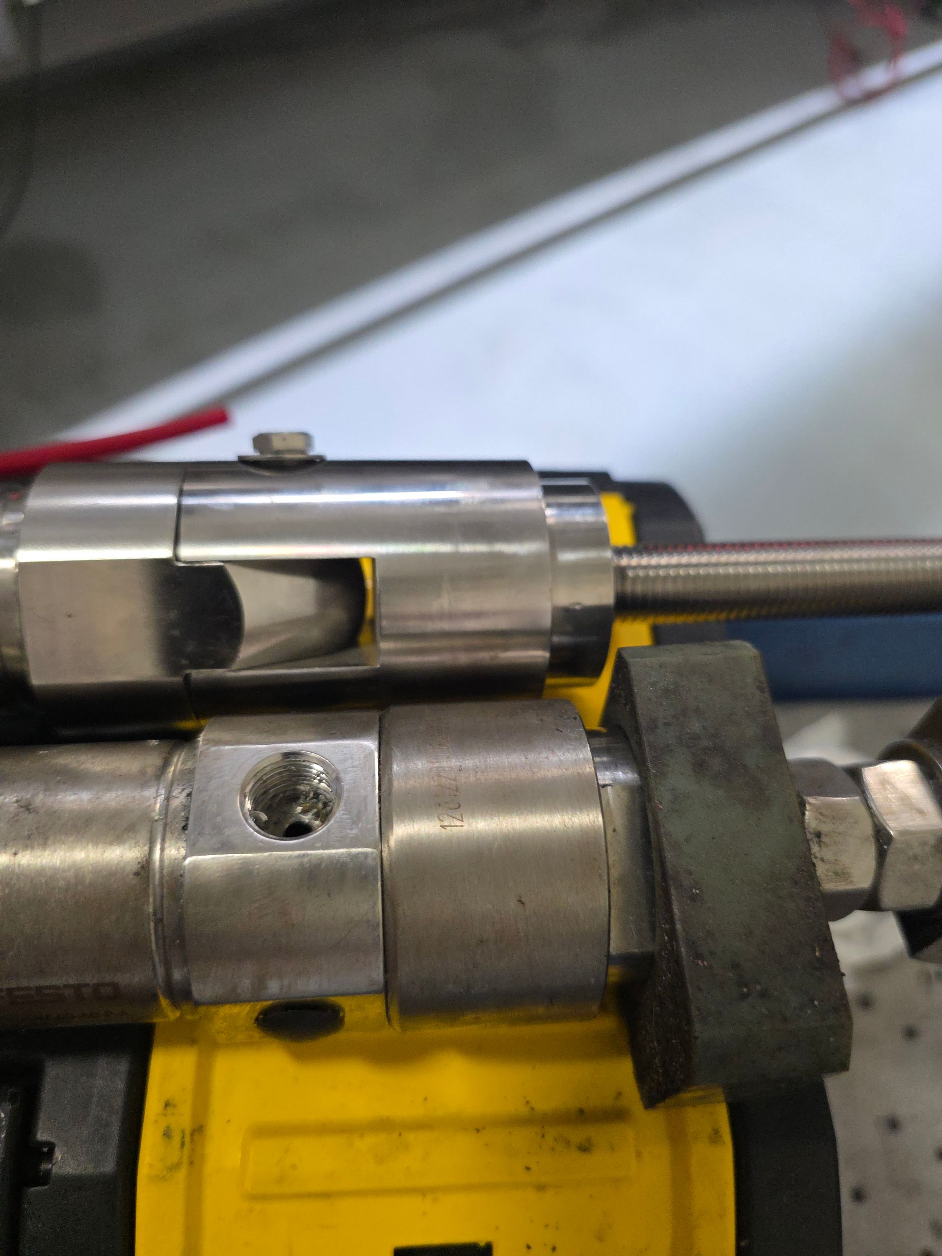 Close-up of two aligned metal couplings with a threaded rod on a yellow machine base.