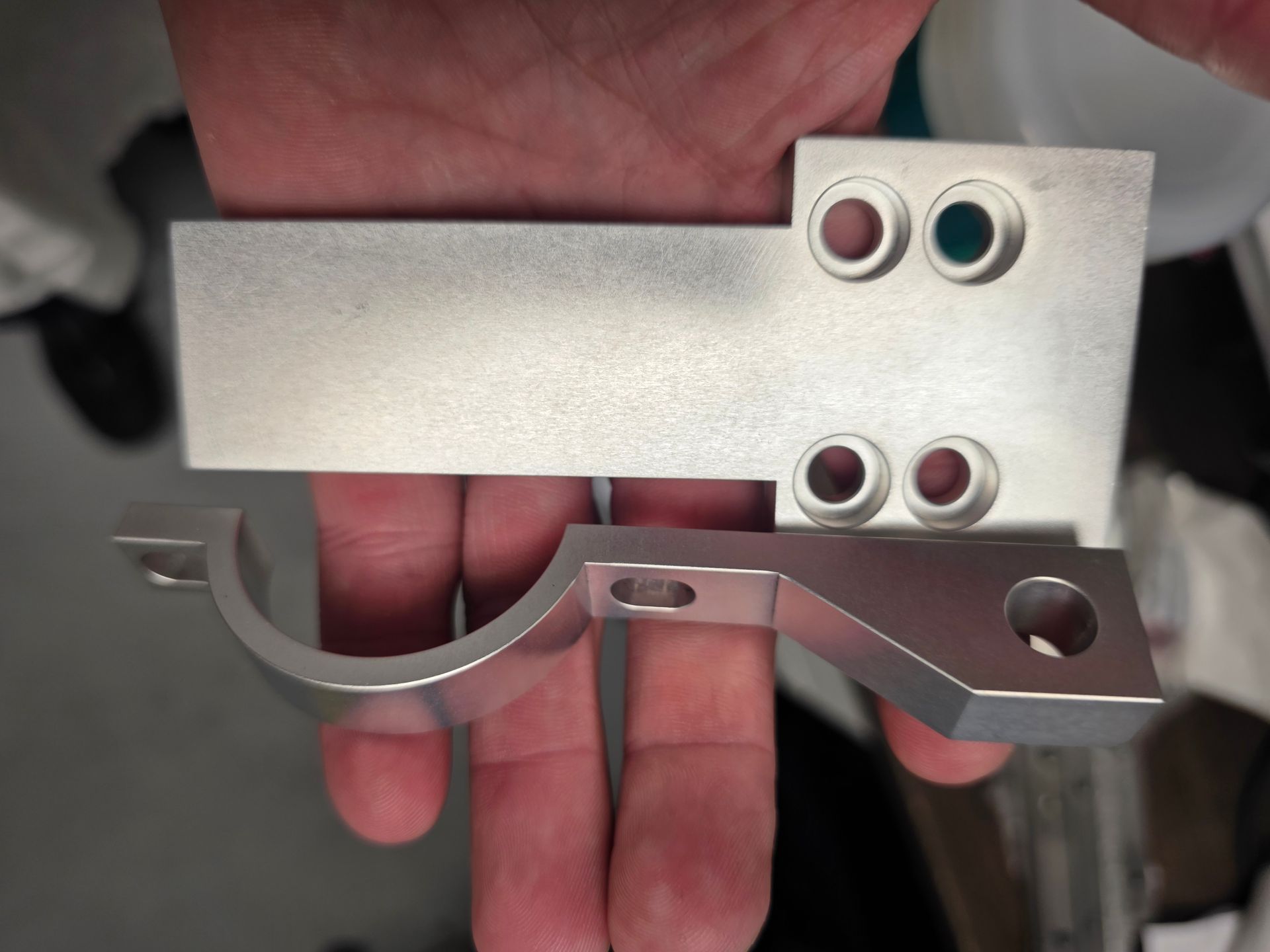 Hand holding a silver metal bracket with curved cutouts and four colored grommet holes