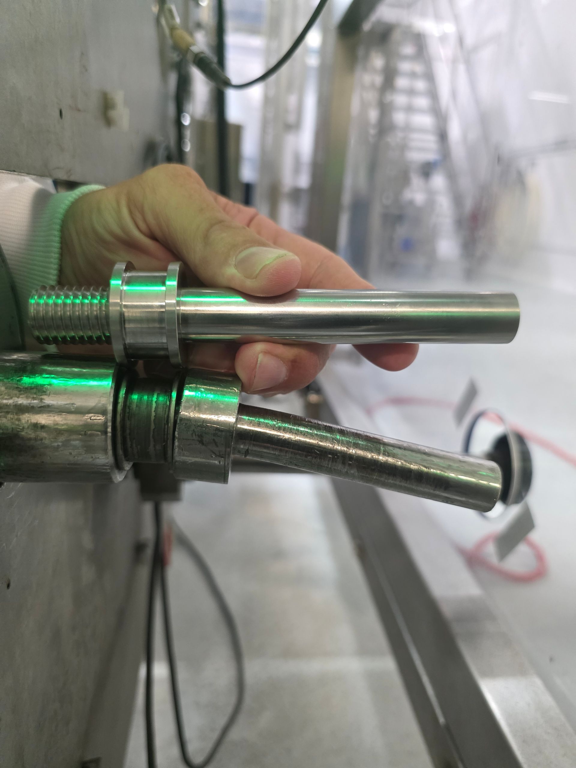 Gloved hand inserting a metal pipe into a fixture in an industrial workshop