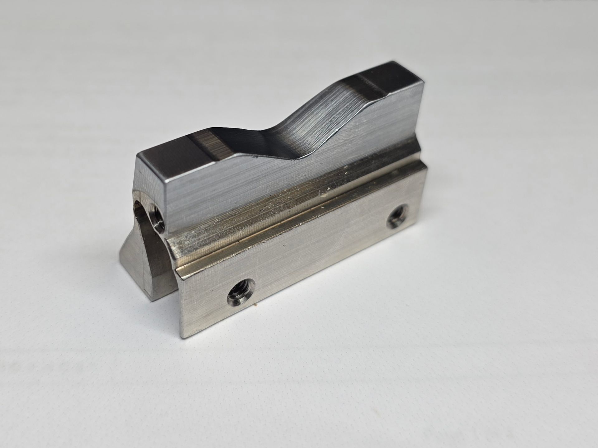 Small metal machined part with a stepped top and two screw holes on a white background