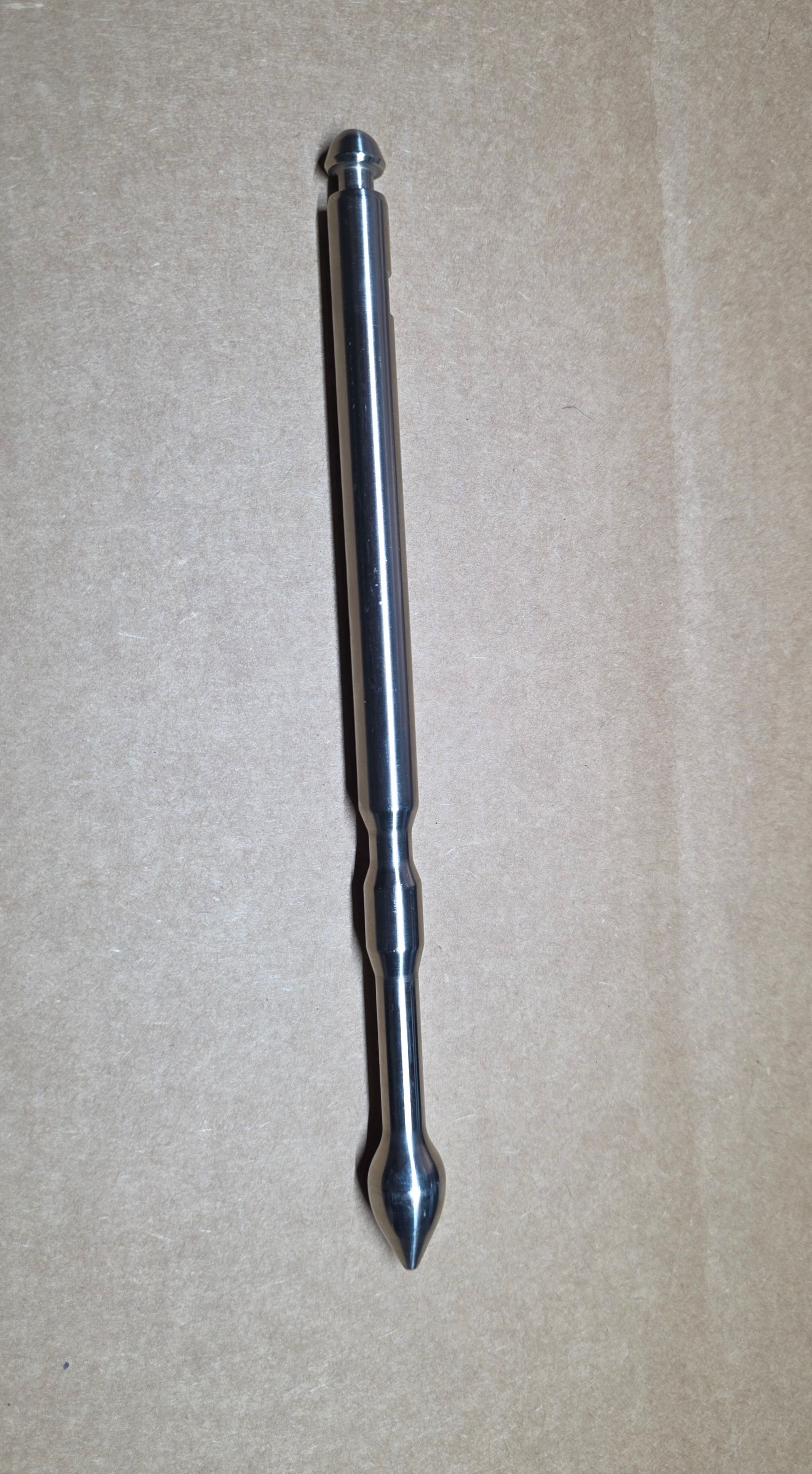 A metal double-ended stylus with a rounded tip on one end and a pointed tip on the other.