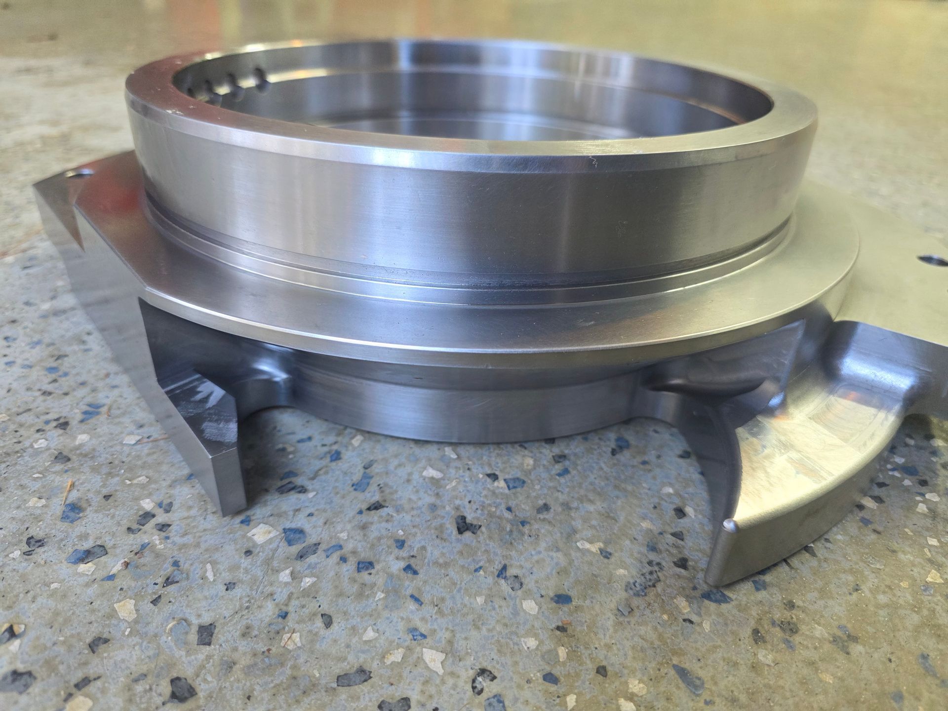 Close-up of a metal machined ring with clamps on a workbench, showing a polished silver finish.