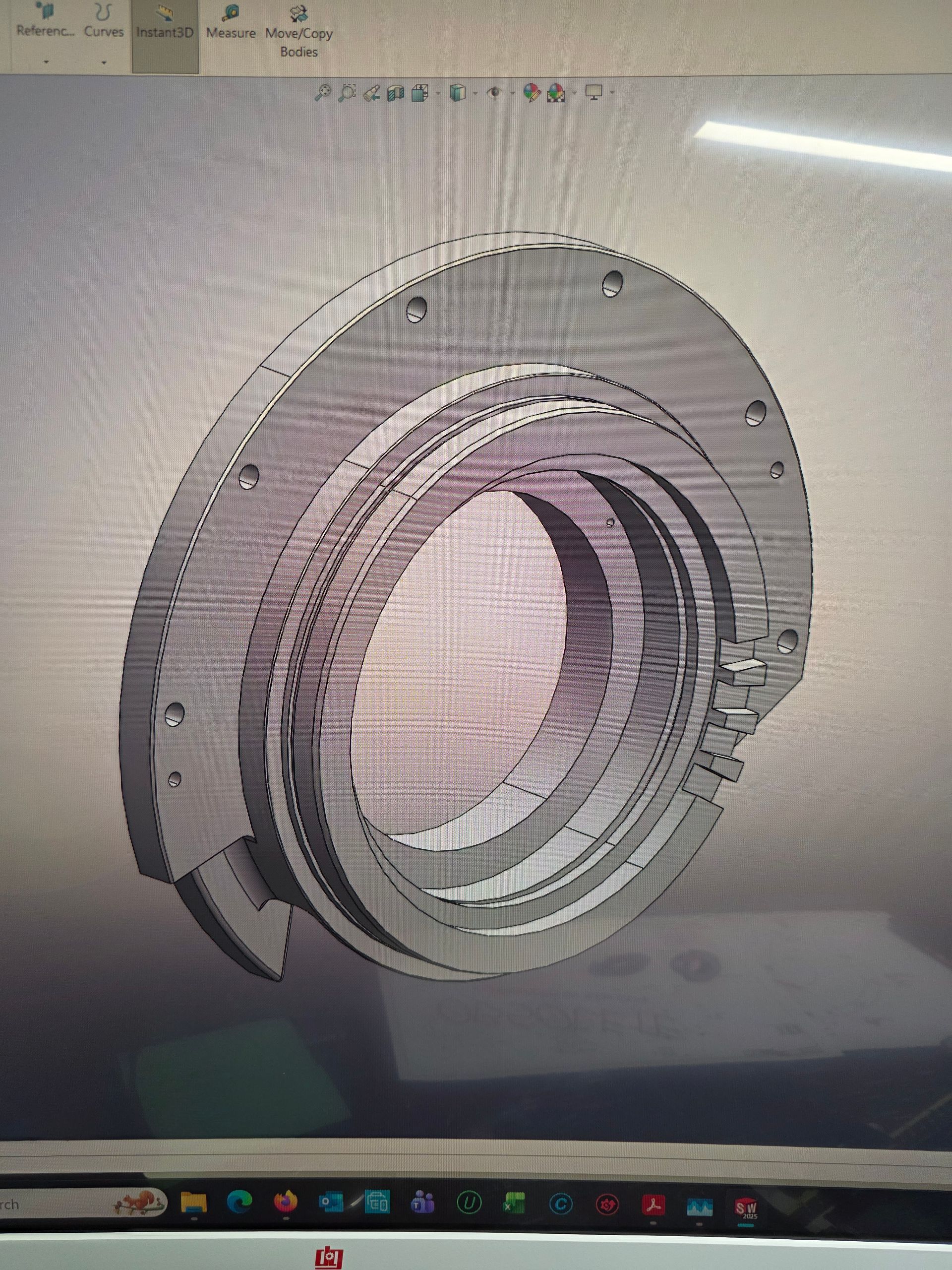 3D CAD rendering of a gray circular mechanical housing with threaded inner rings and bolt holes