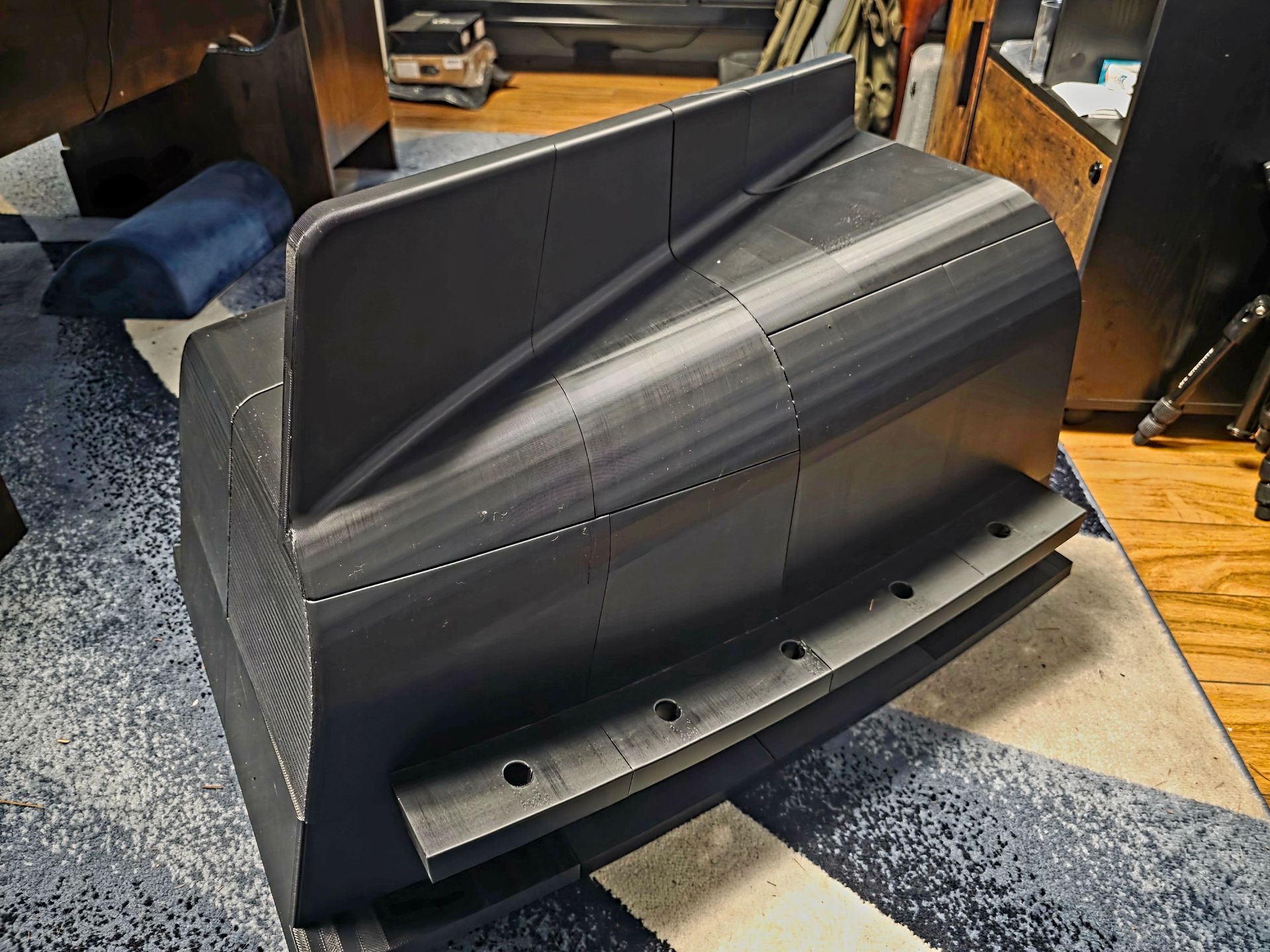 Black plastic snowplow blade attachment in a workshop, with mounting holes and curved edge