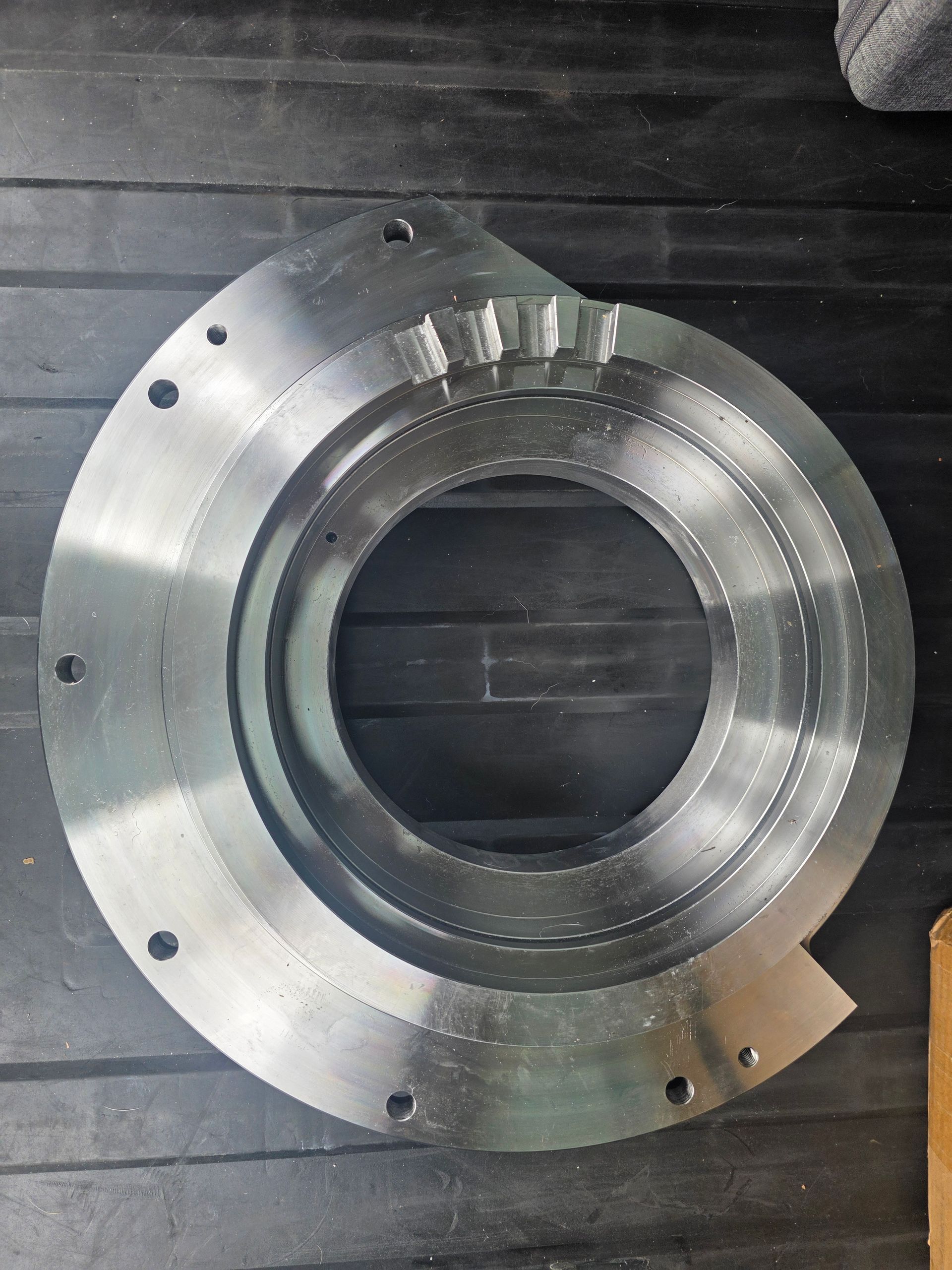 Silver metal bearing housing ring on a dark surface, with bolt holes and machined grooves