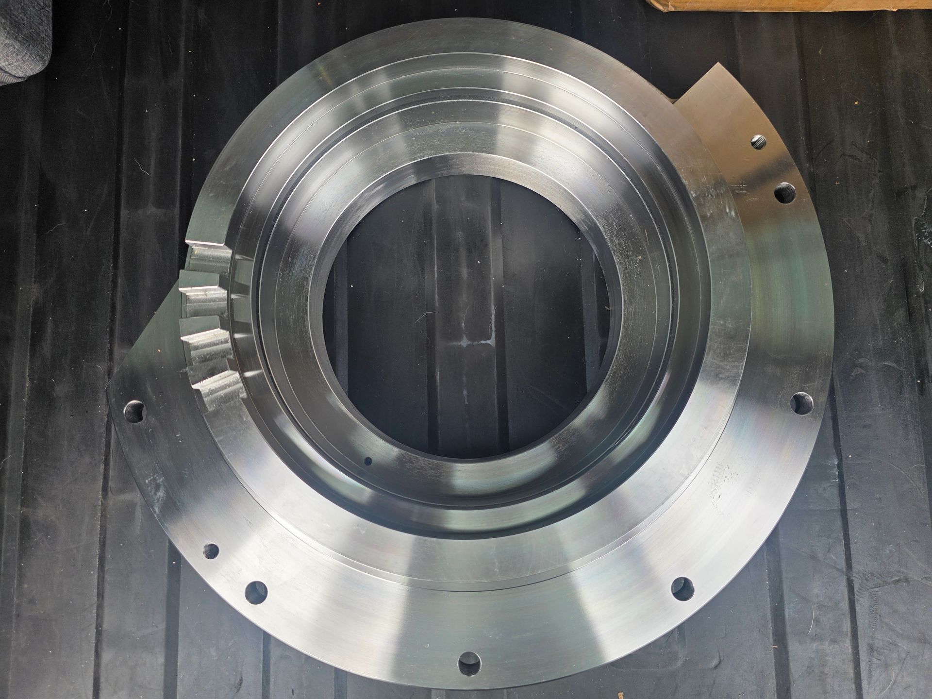 Close-up of a shiny metal circular machined part with bolt holes on a dark surface