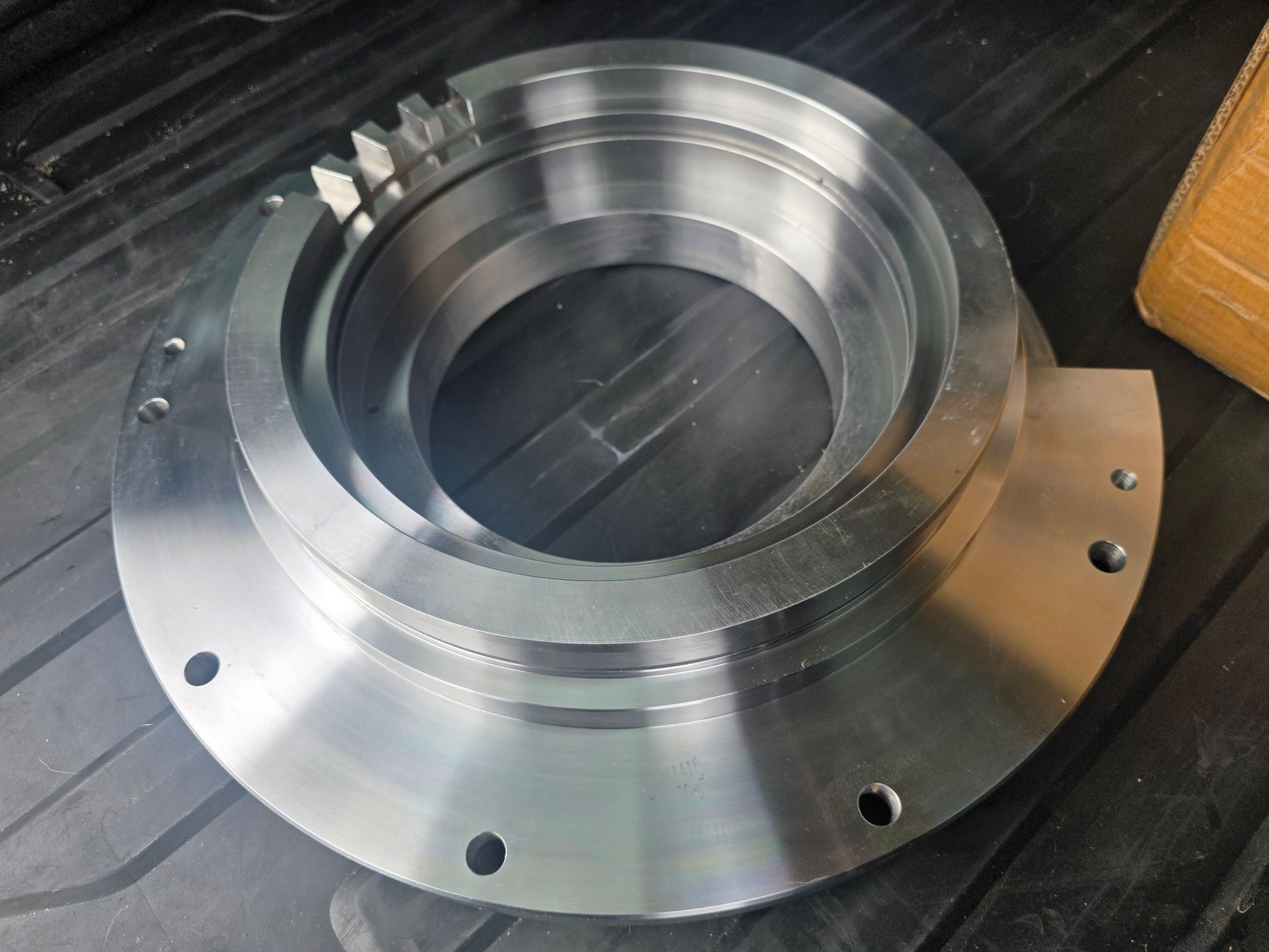 Machined metal flange with circular bolt holes and a central bore on a dark surface