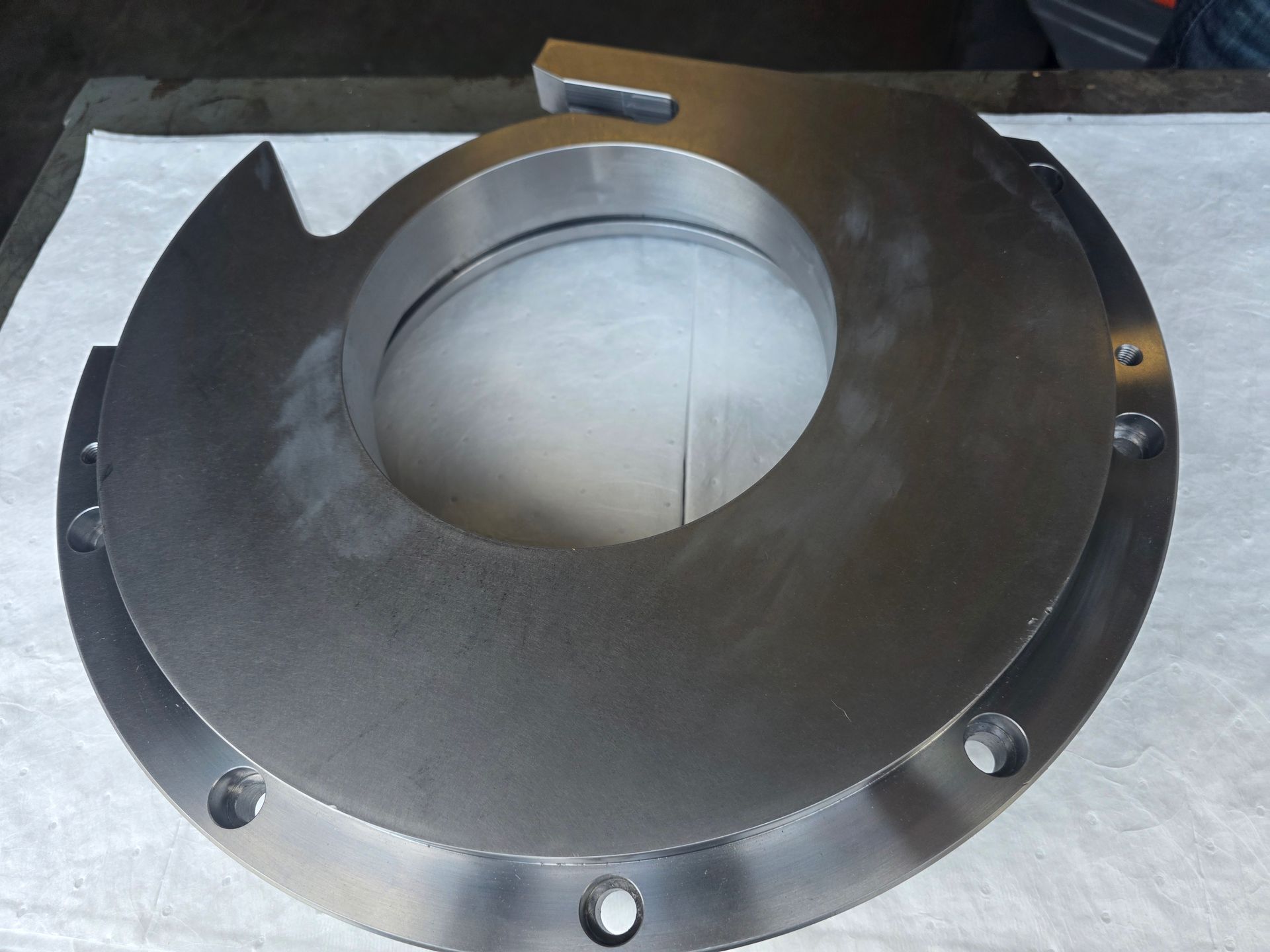 Metal circular housing with a large central opening and bolt holes on a gray surface
