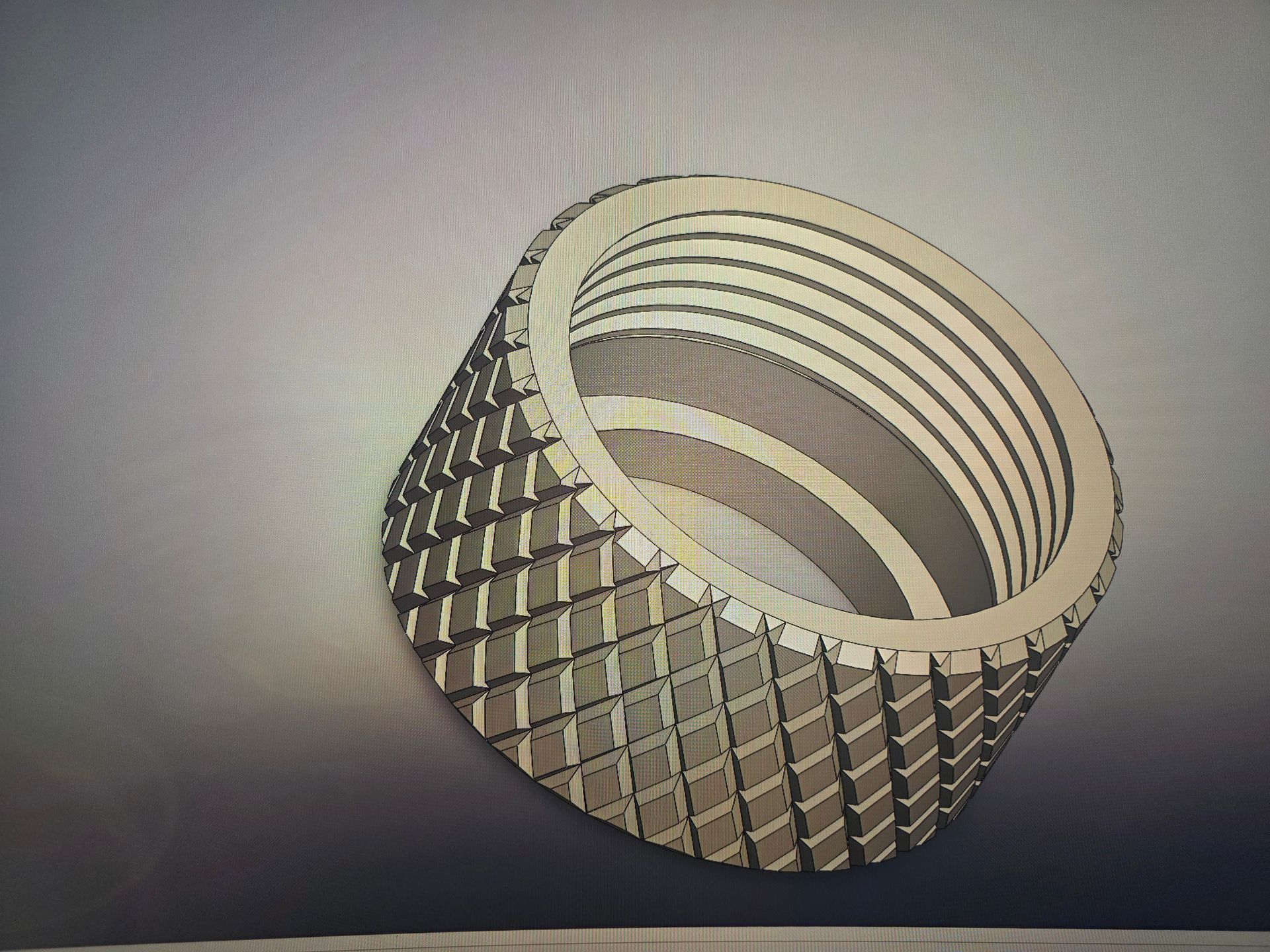 Gray cylindrical woven metal ring with concentric ridges, shown on a plain background