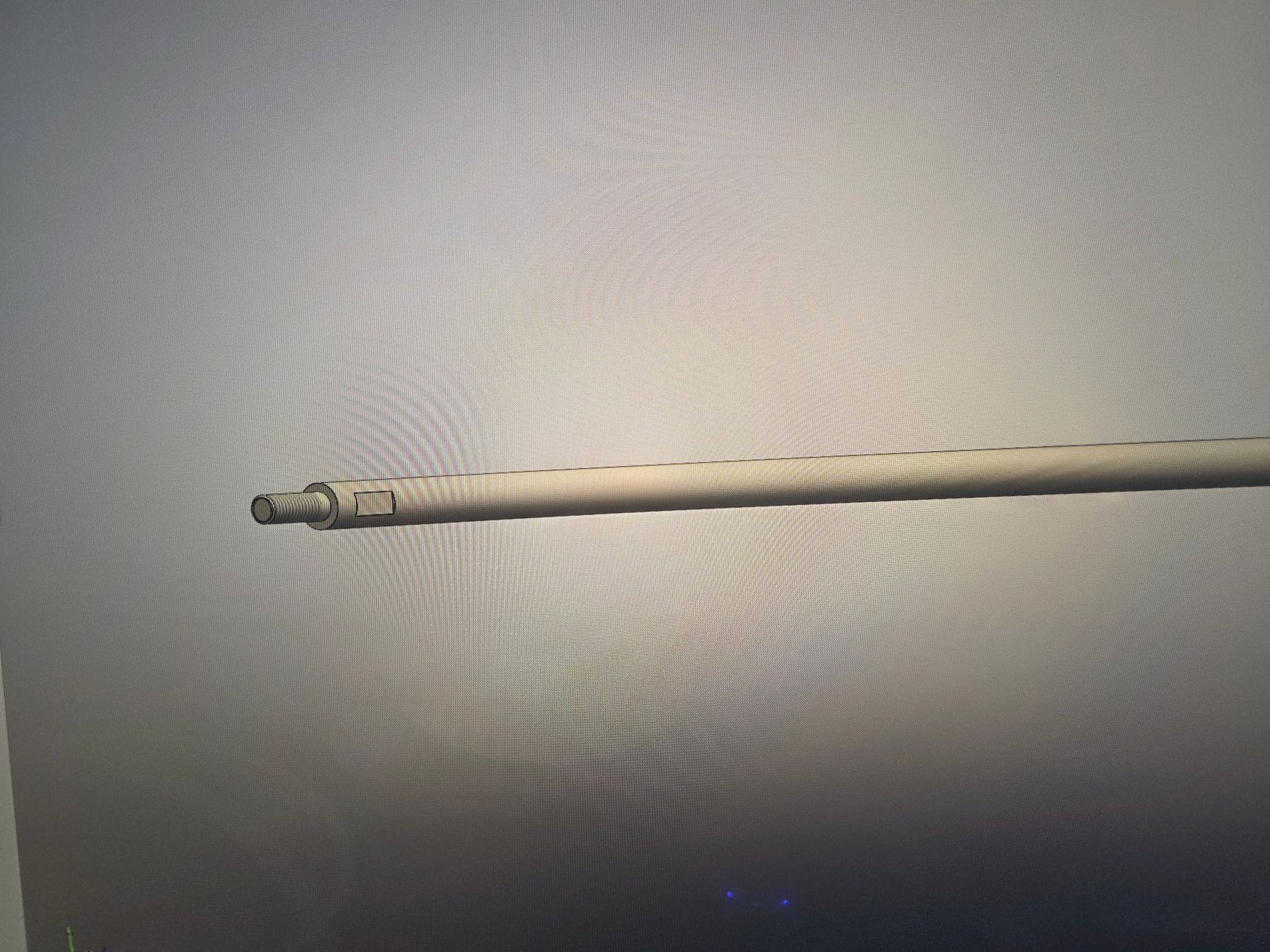 A long beige rod or pipe lying horizontally on a gray surface.