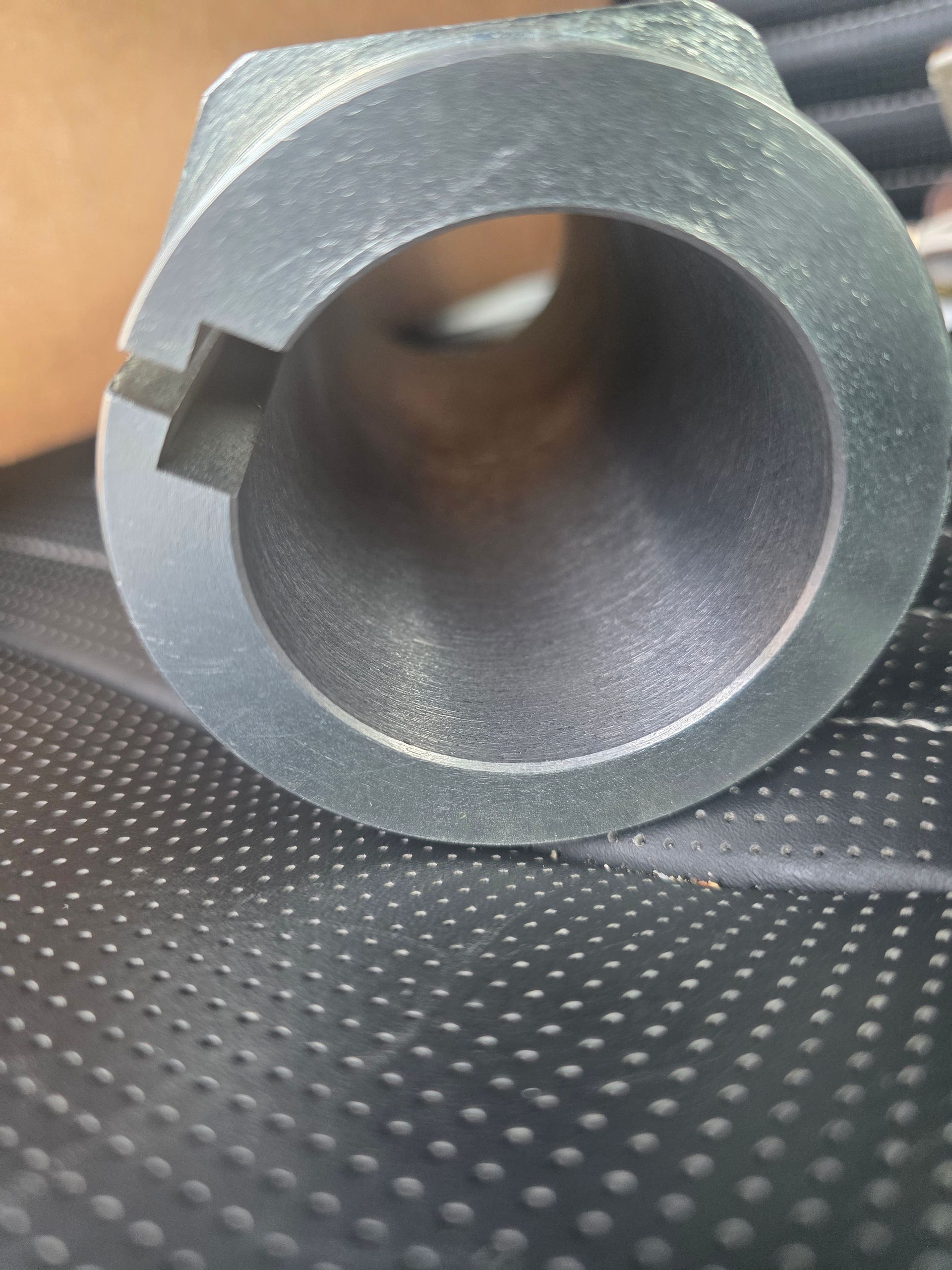 Close-up of a gray cylindrical metal pipe fitting with a circular opening on a textured surface.