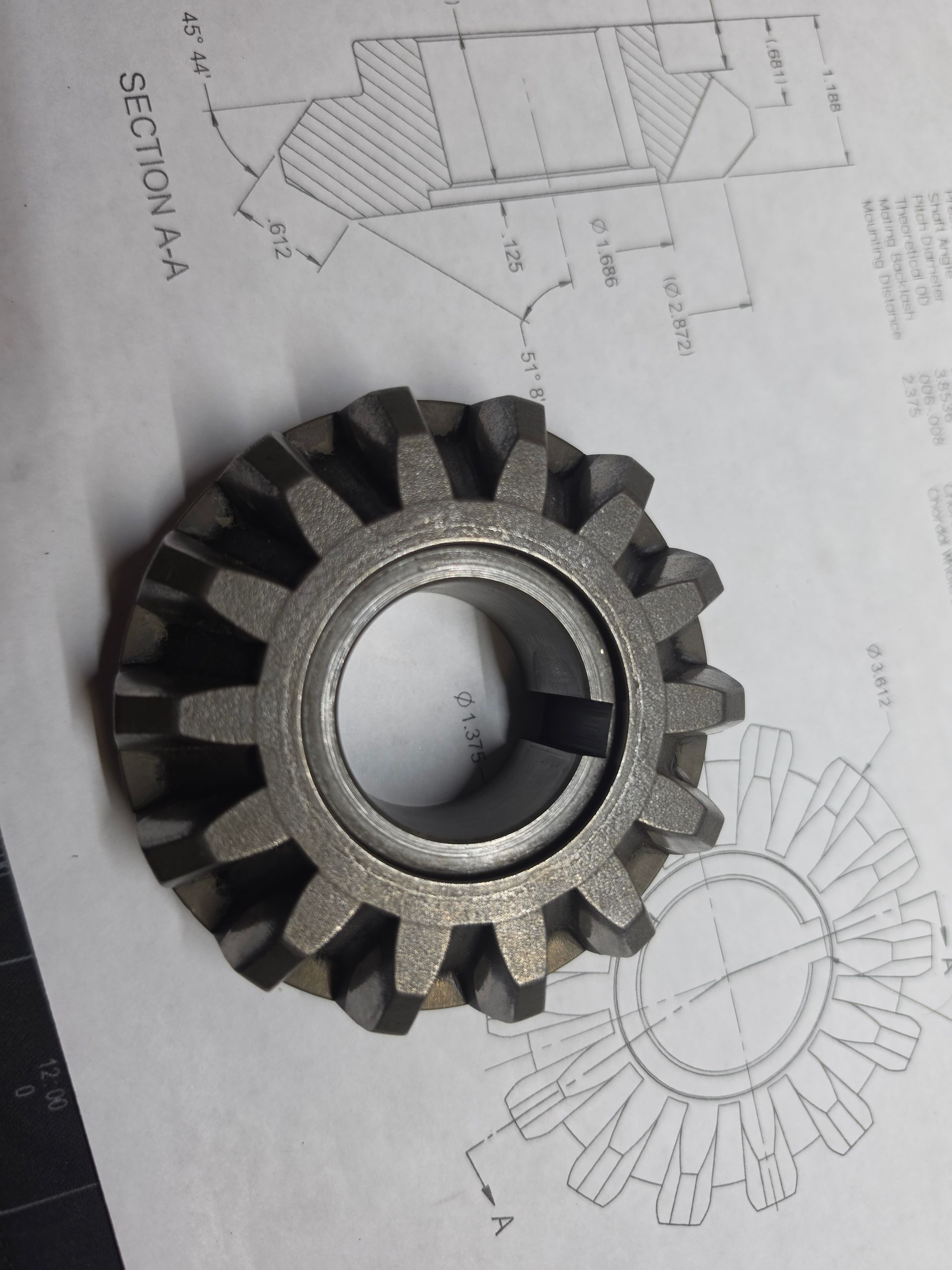 Metal gear wheel on top of a technical drawing sheet.