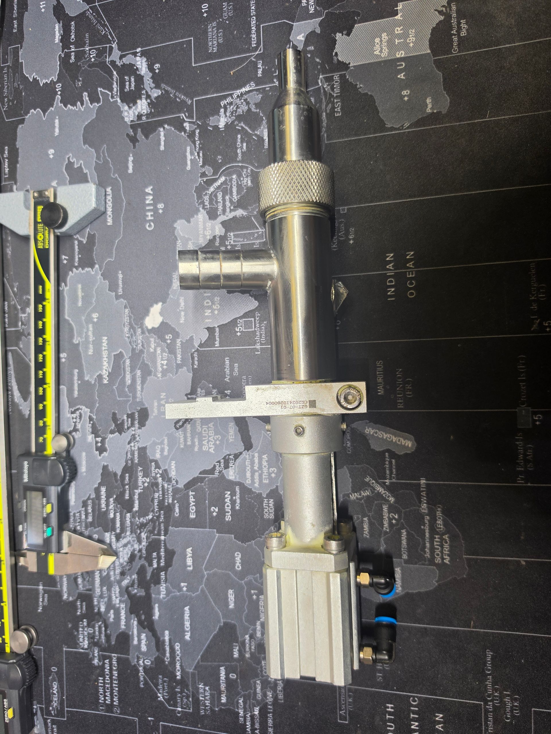 Metal pipe assembly on a patterned surface, with a clamp and ruler beside it.