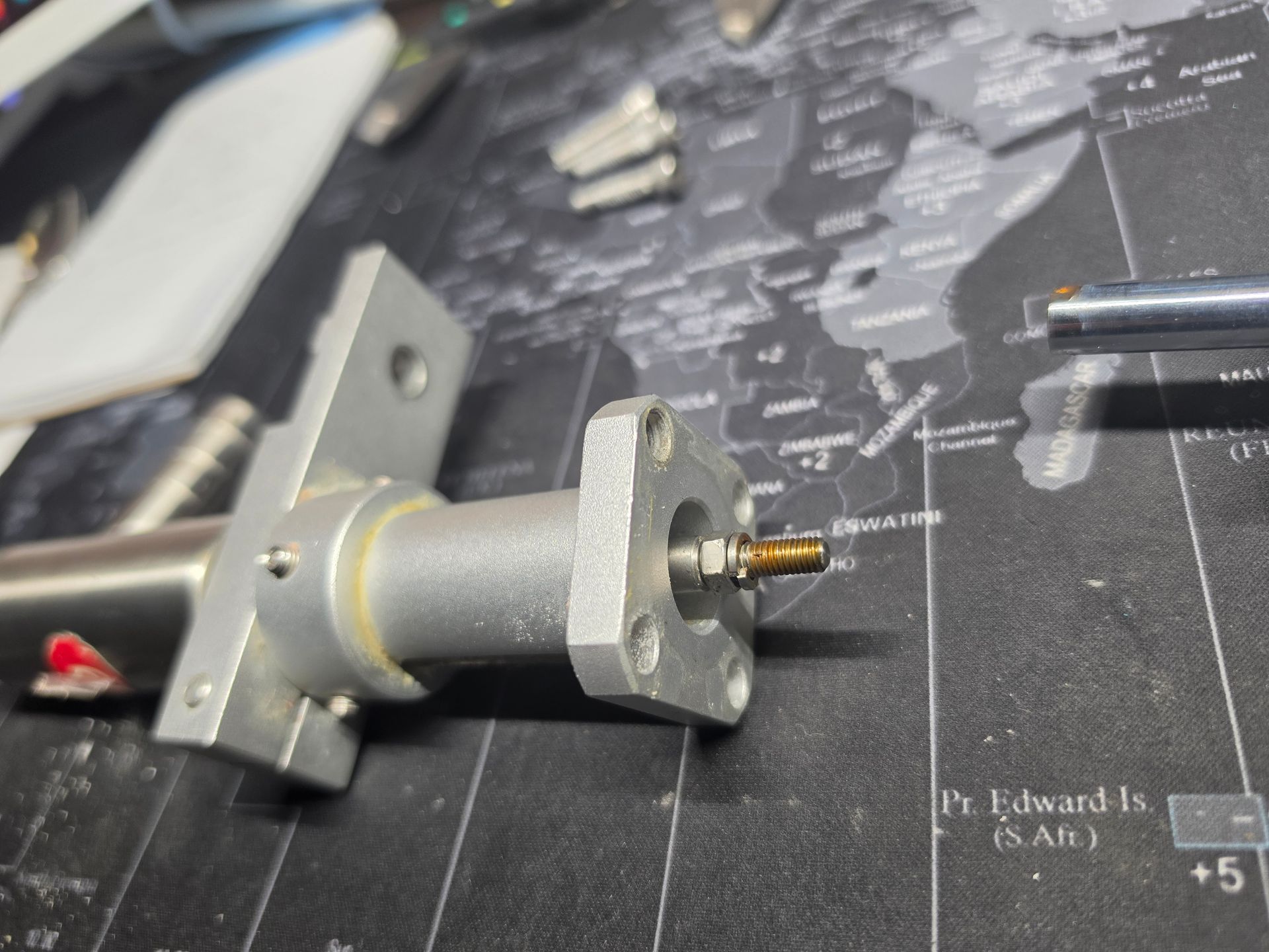 Close-up of a metal mechanical component on a dark workbench mat with small tools nearby