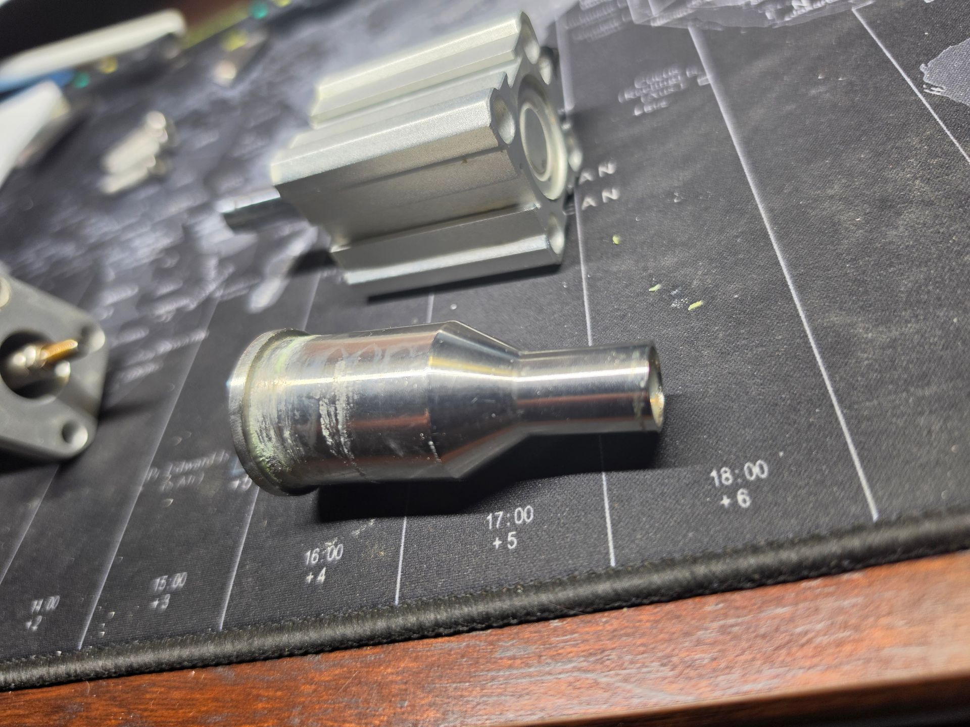 Metal tool bits on a black measuring mat with a wooden edge; one shiny tapered piece in the foreground.