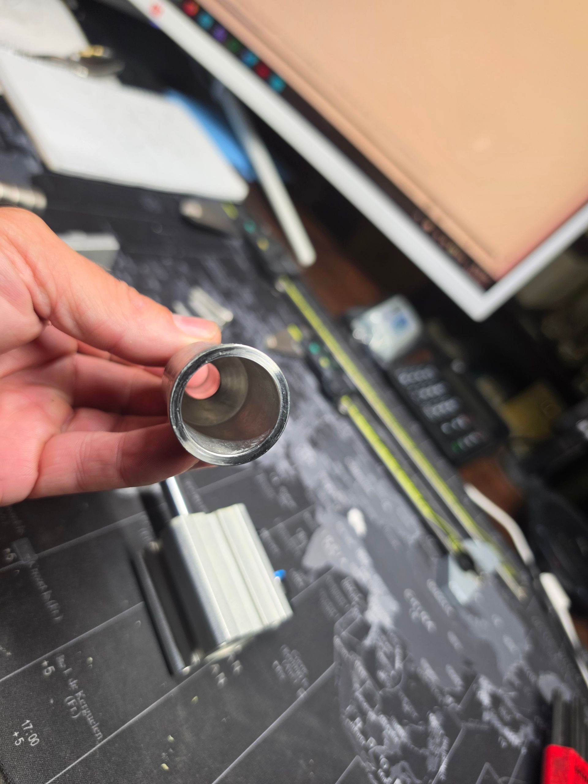 Hand holding a small metal ring over a cluttered workbench with tools and a monitor in the background