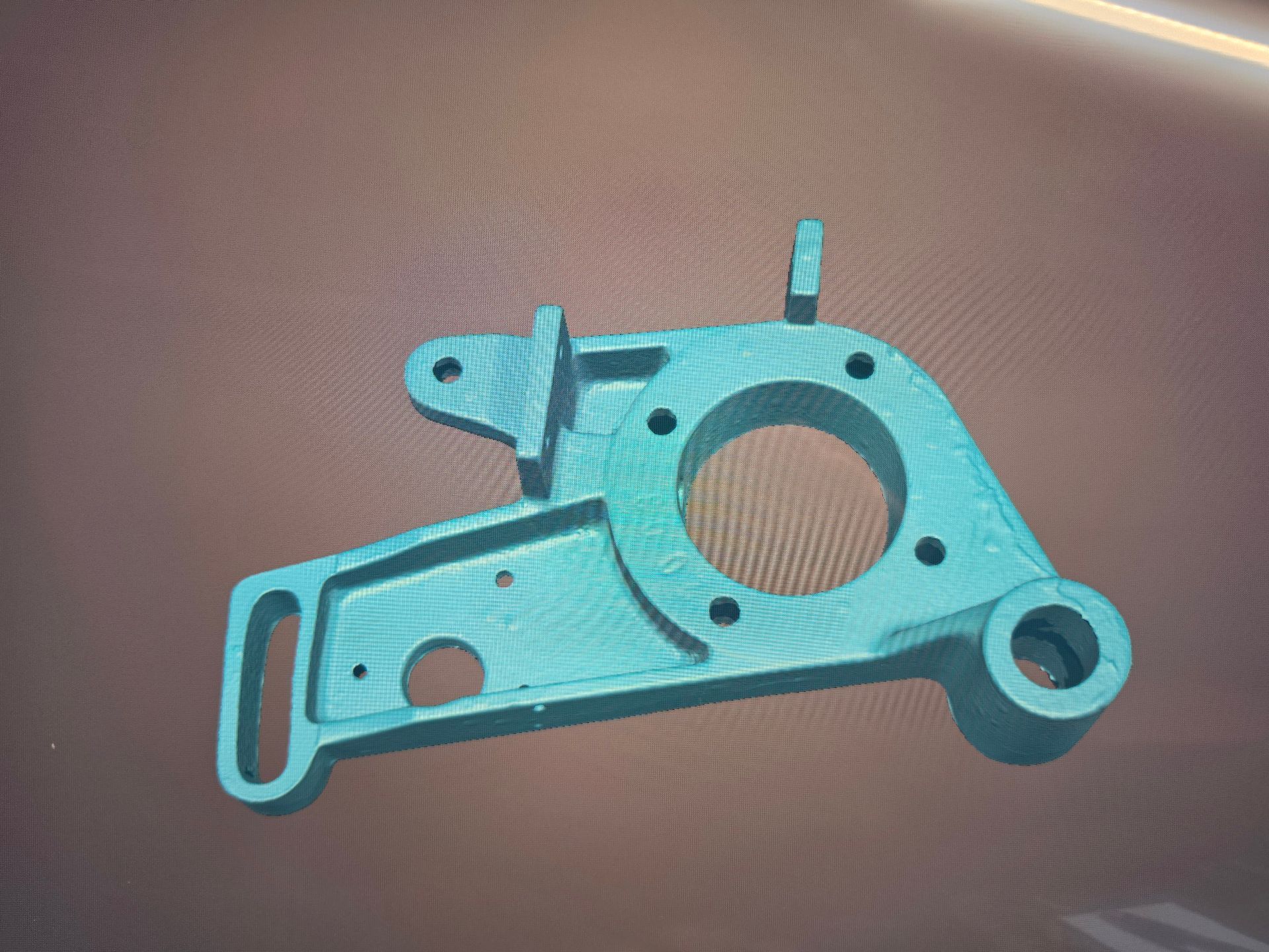 Turquoise machined metal bracket with holes and slots on a brown surface