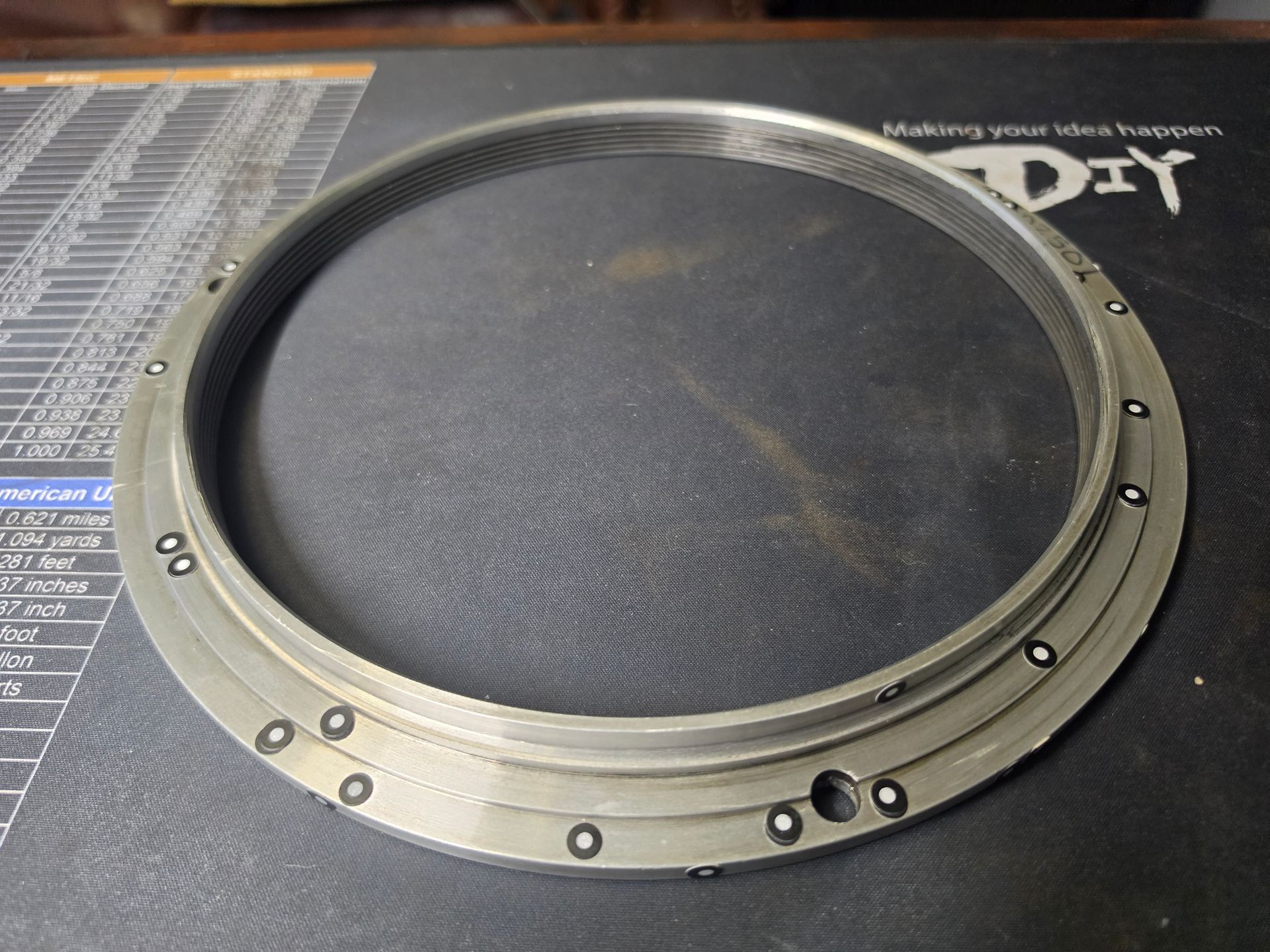 Close-up of a large speaker driver with a black cone and silver mounting ring on a workbench