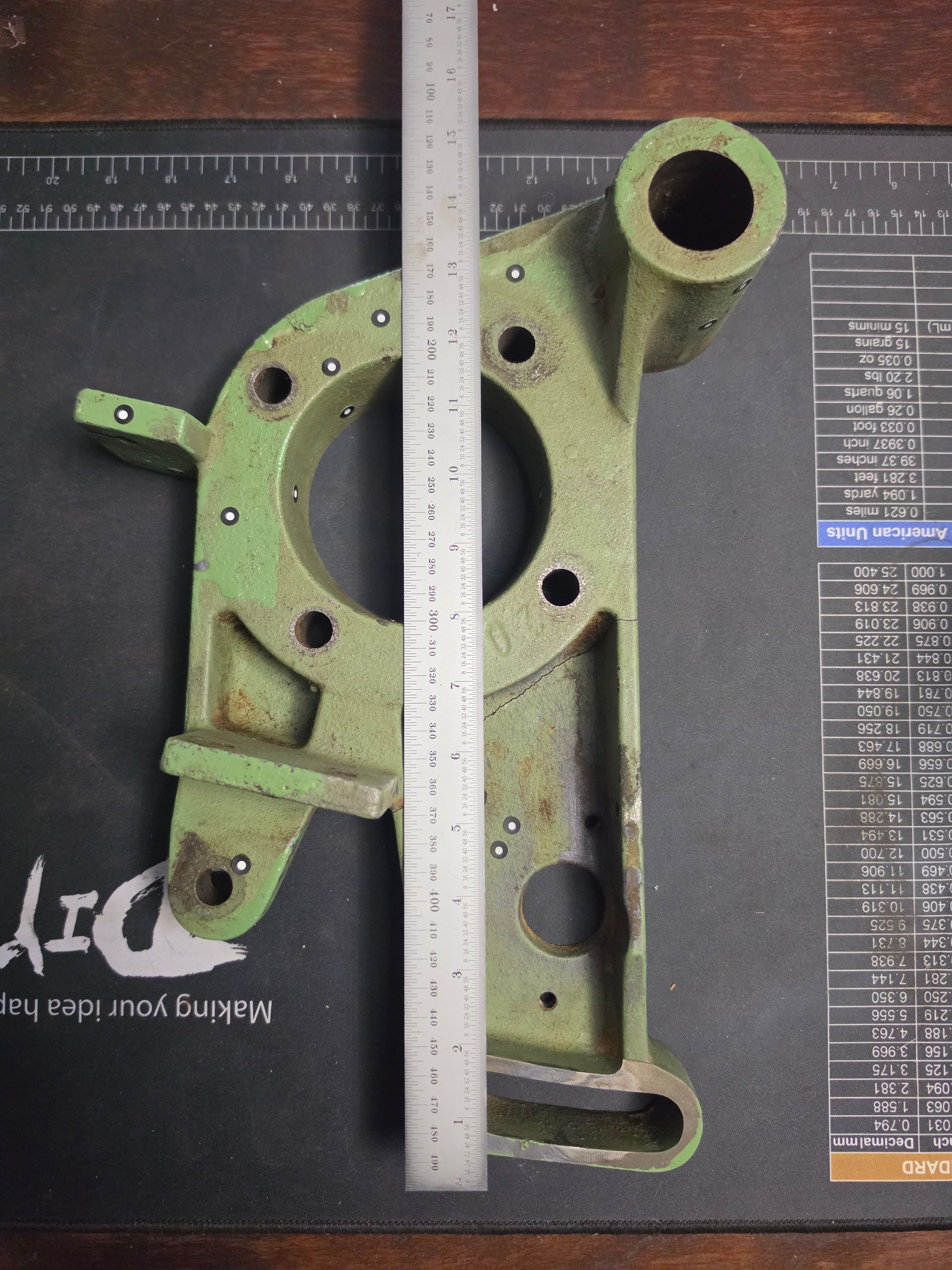Green cast-metal mechanical bracket with a ruler laid vertically beside it on a dark surface.