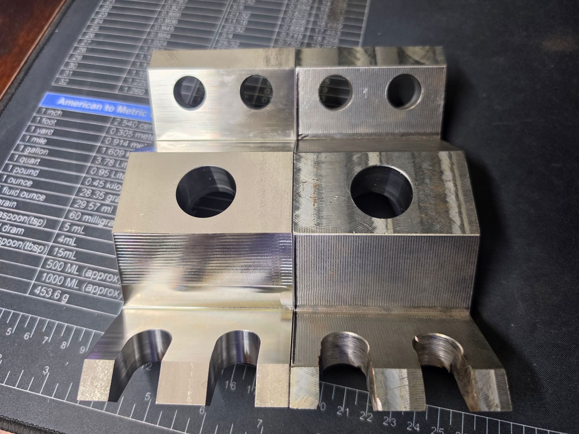 Stacked aluminum machining test blocks with drilled holes and cutouts on a dark work mat