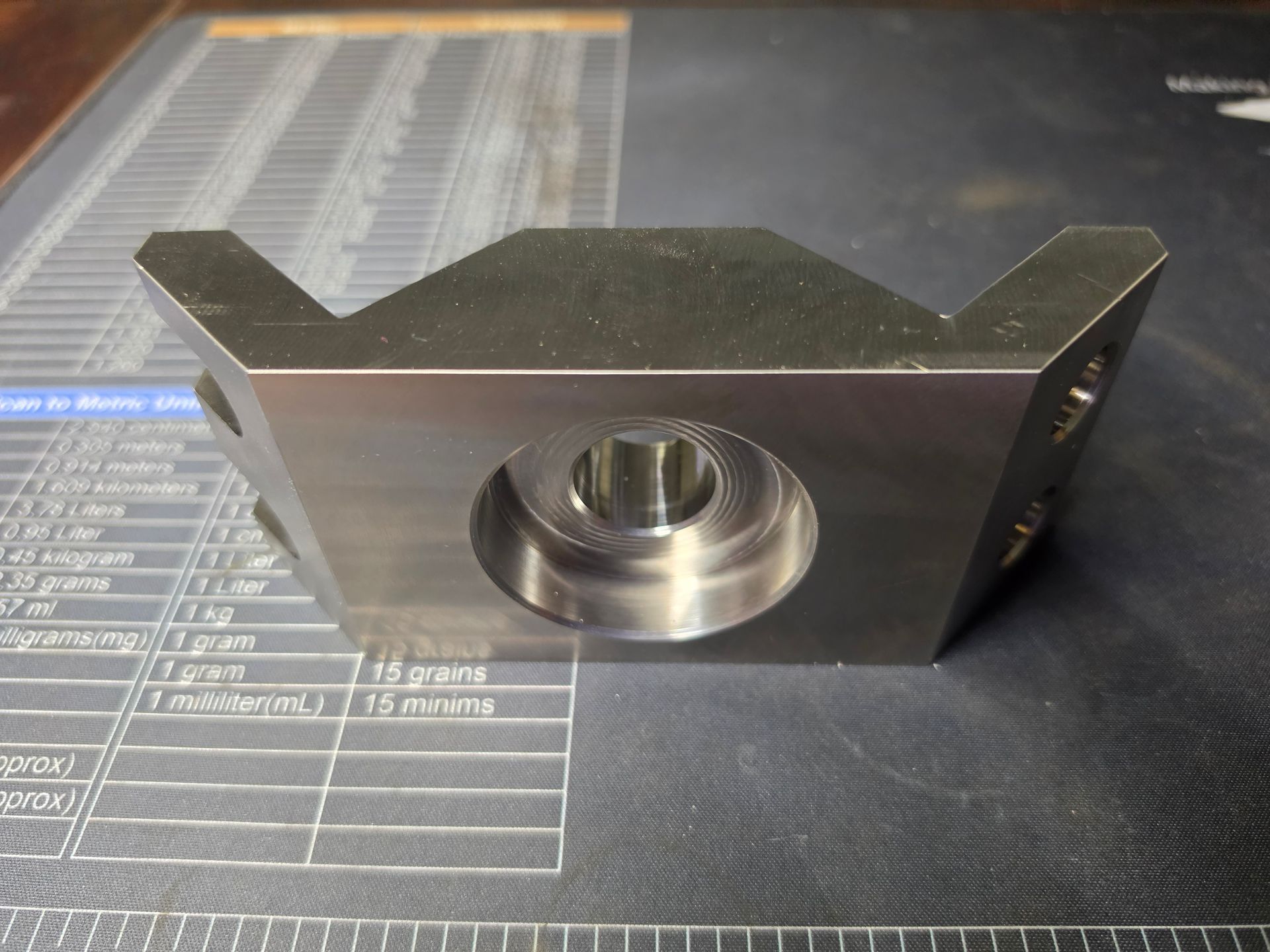 Metal machined part with a central hole resting on a printed measurement mat.