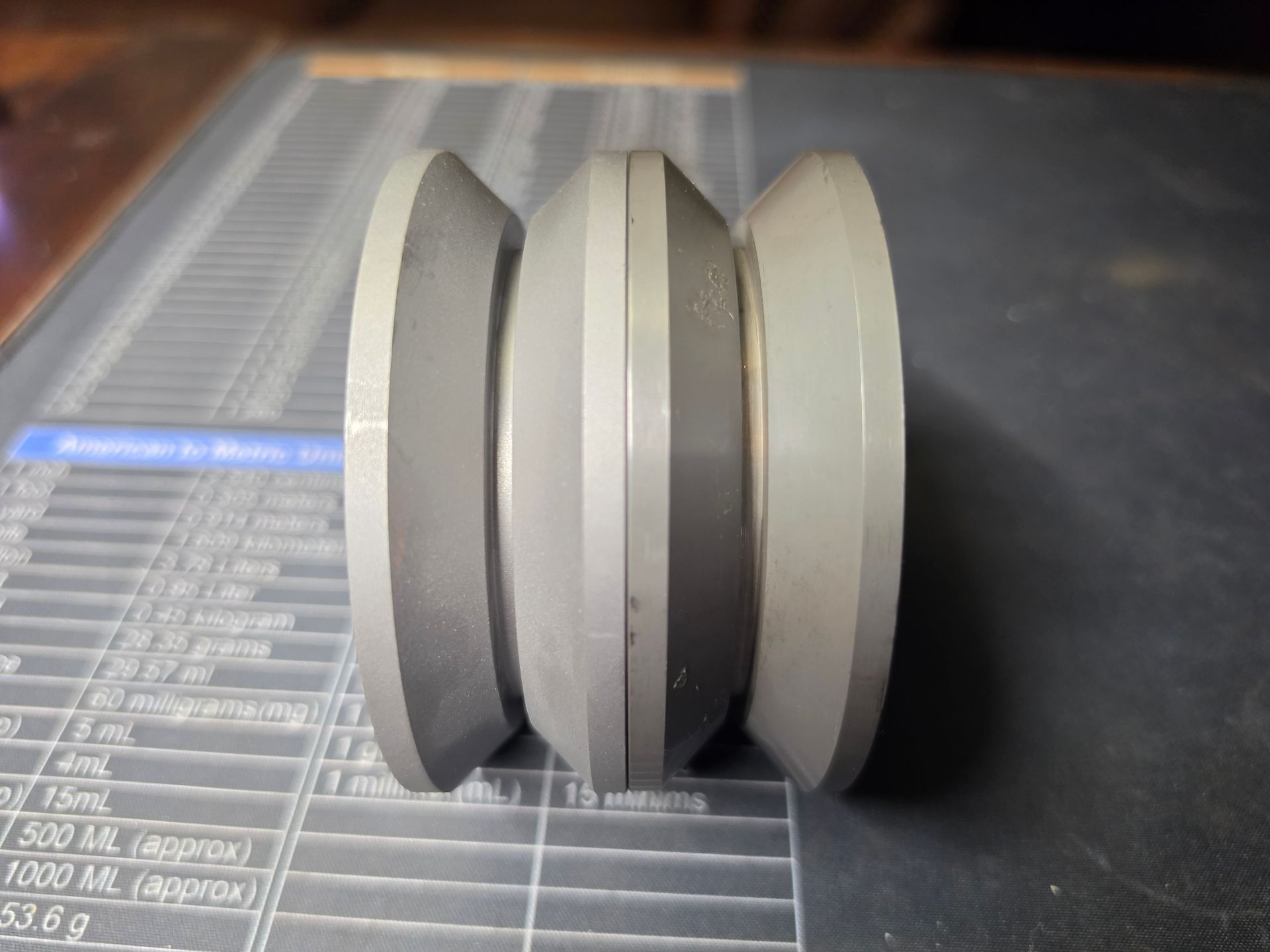 Close-up of a gray double-groove pulley wheel on a dark patterned surface.