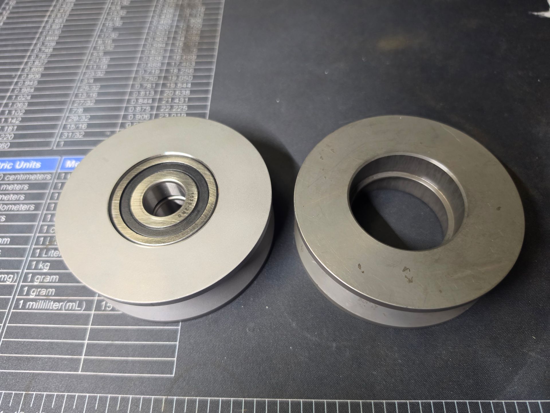 Two metal pulley wheels on a dark mat, one with a bearing visible in the center